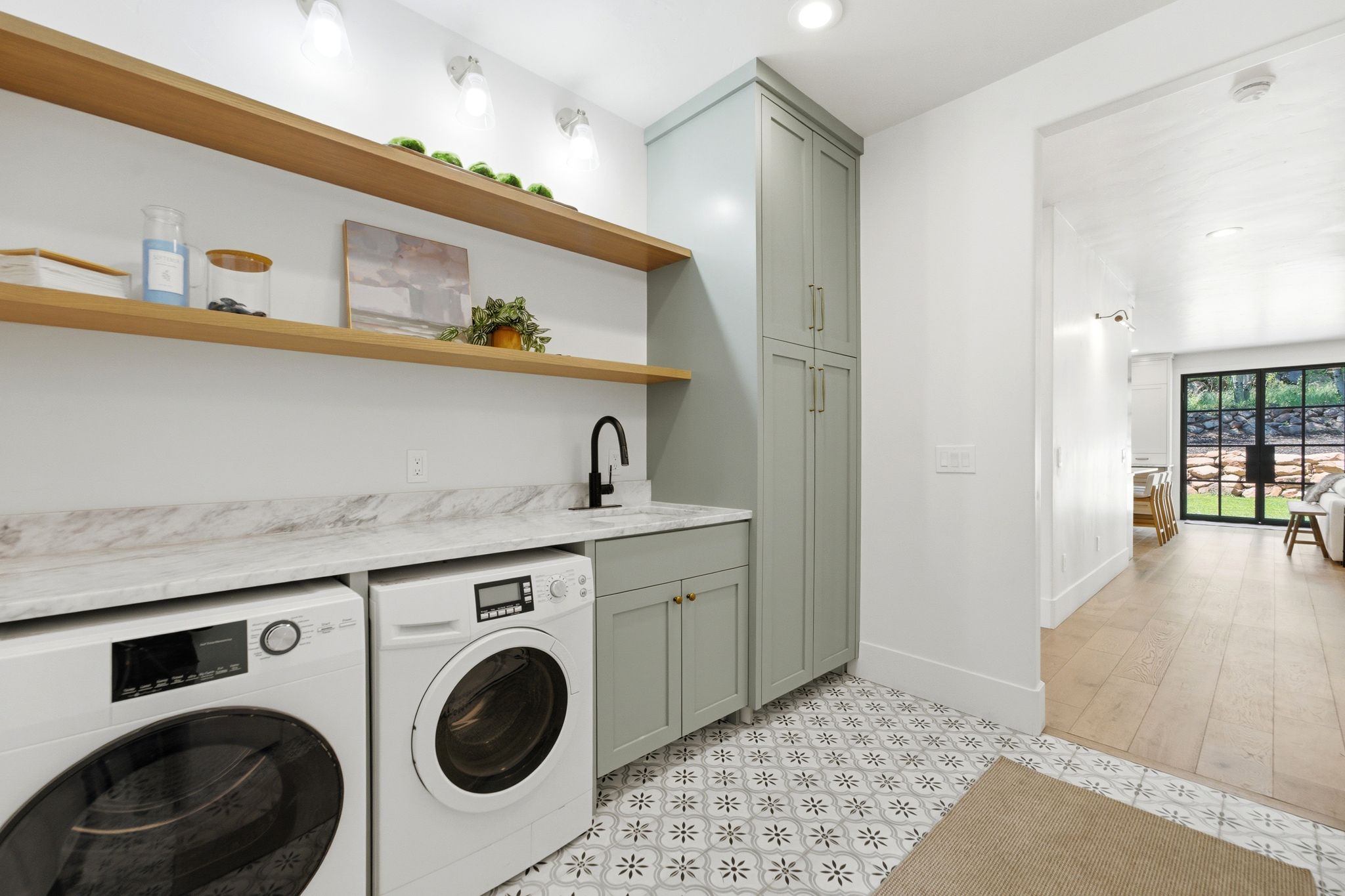 Laundry area featuring stacked wood shelving, light green cabinetry, a countertop with an undermount sink, and patterned floor tiling