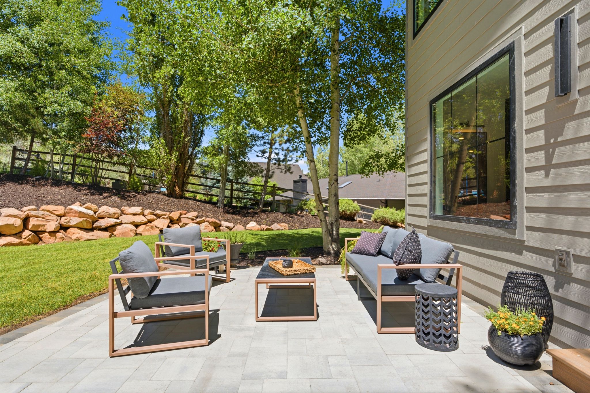 Expansive paved patio with a horizontal siding exterior, large black-trimmed windows, and exterior sconce lighting