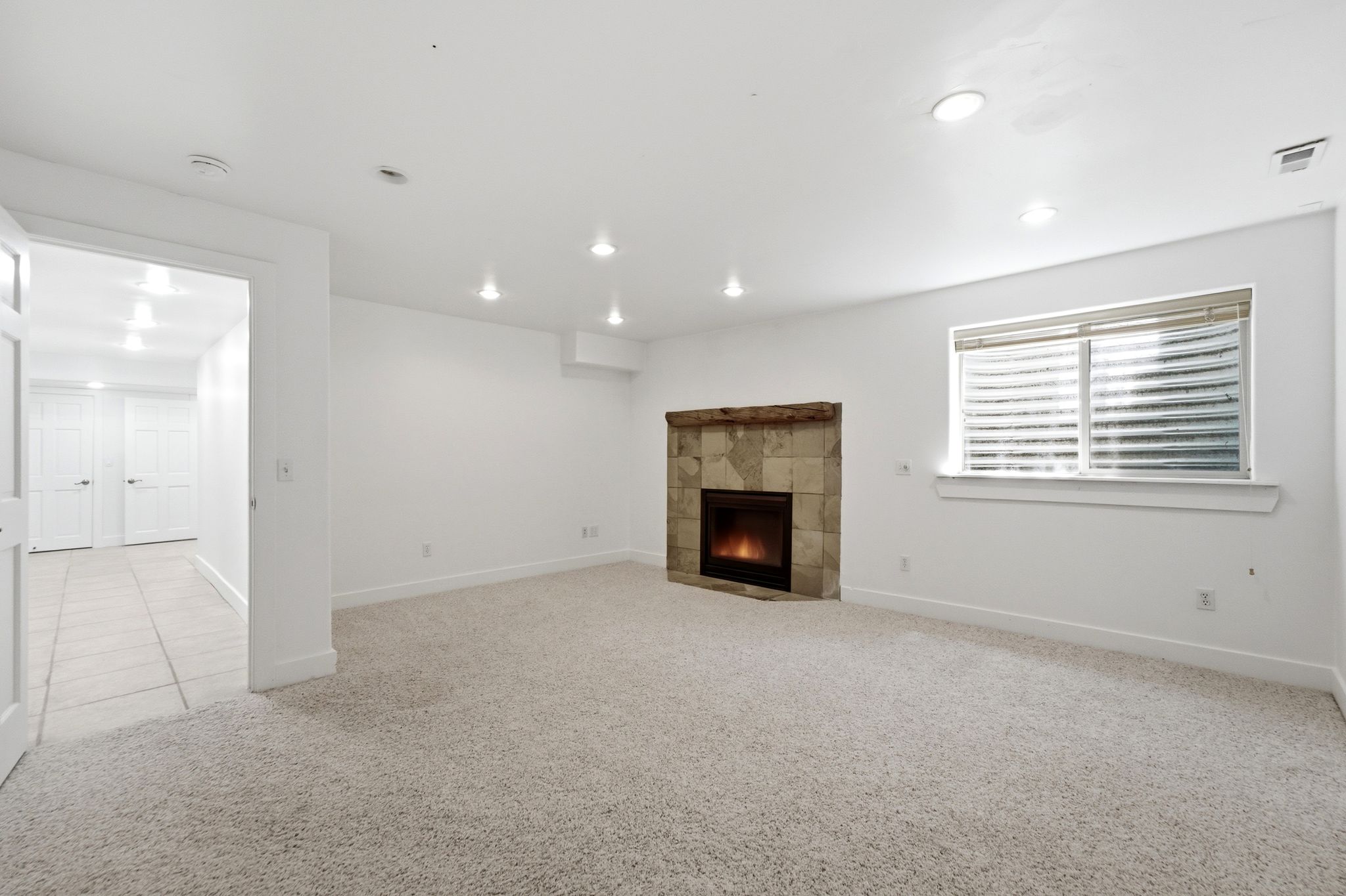 Spacious room featuring light-toned carpeting and a corner fireplace with stone surround and wood mantel
