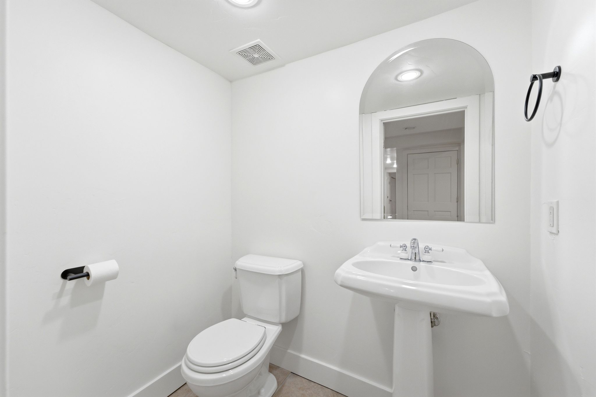 Pedestal sink with chrome faucet, arched wall mirror, and recessed lighting