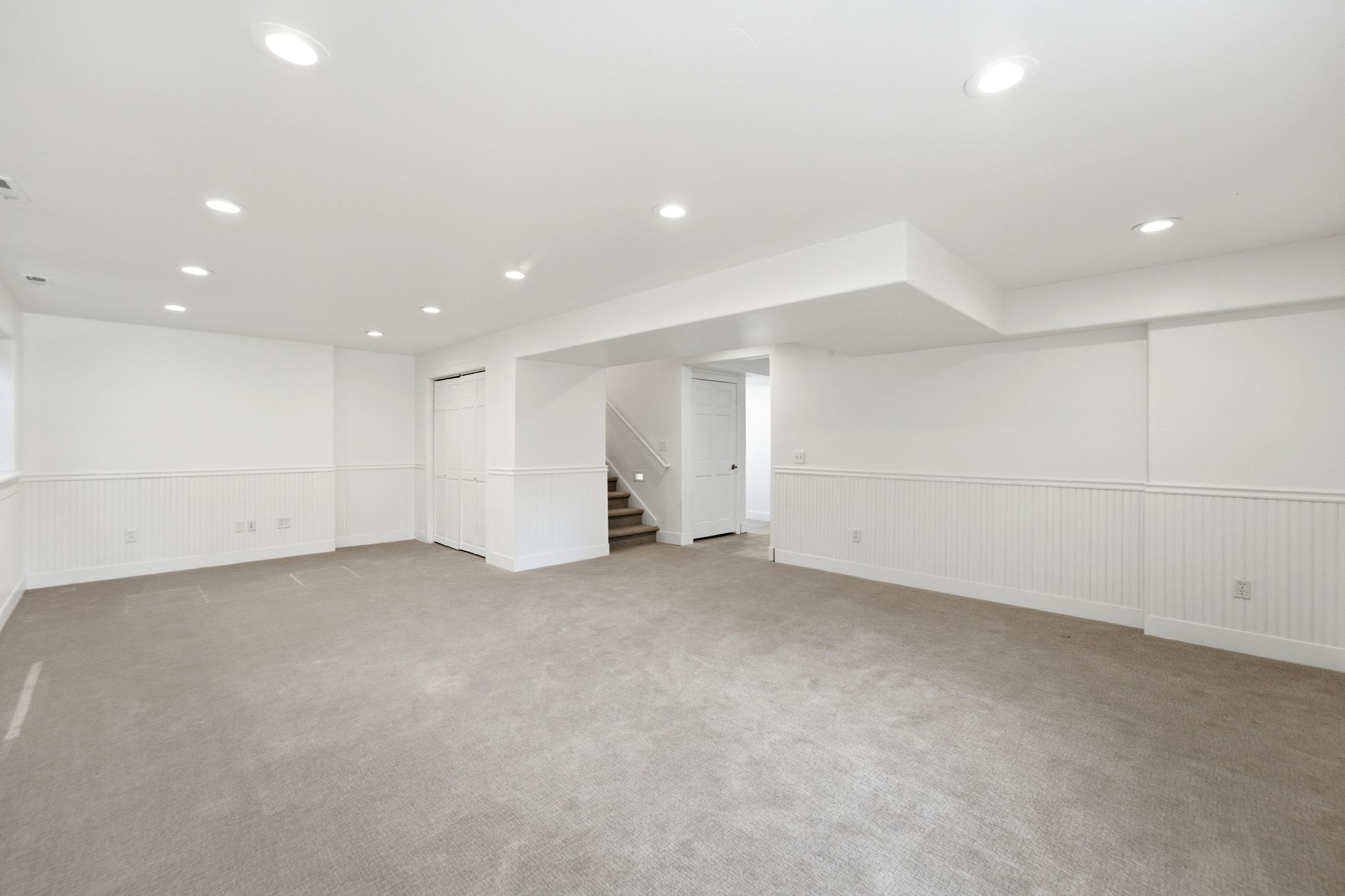 Expansive carpeted room featuring white beadboard wainscoting, recessed lighting, and a neutral color palette