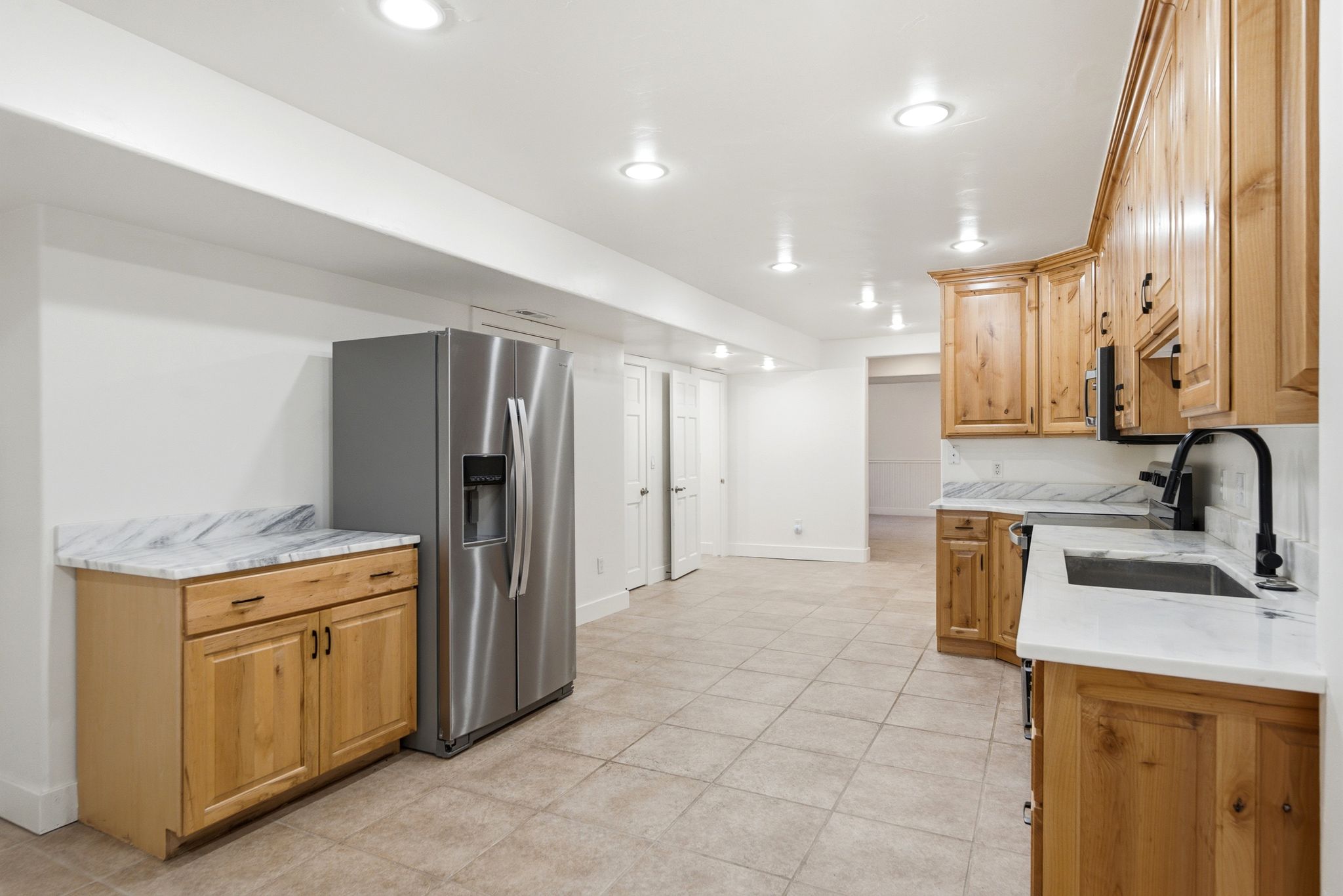 Kitchenette featuring natural wood cabinetry, light-toned tiled flooring, white countertops with veining, a stainless steel refrigerator, and recessed lighting