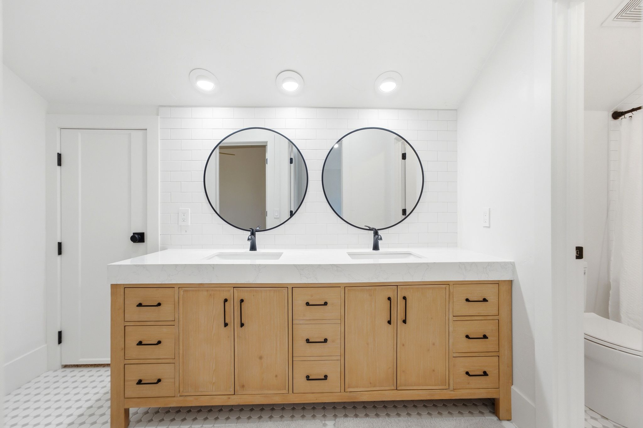 Dual vanity featuring natural wood cabinetry, white countertop, and two round black-framed mirrors