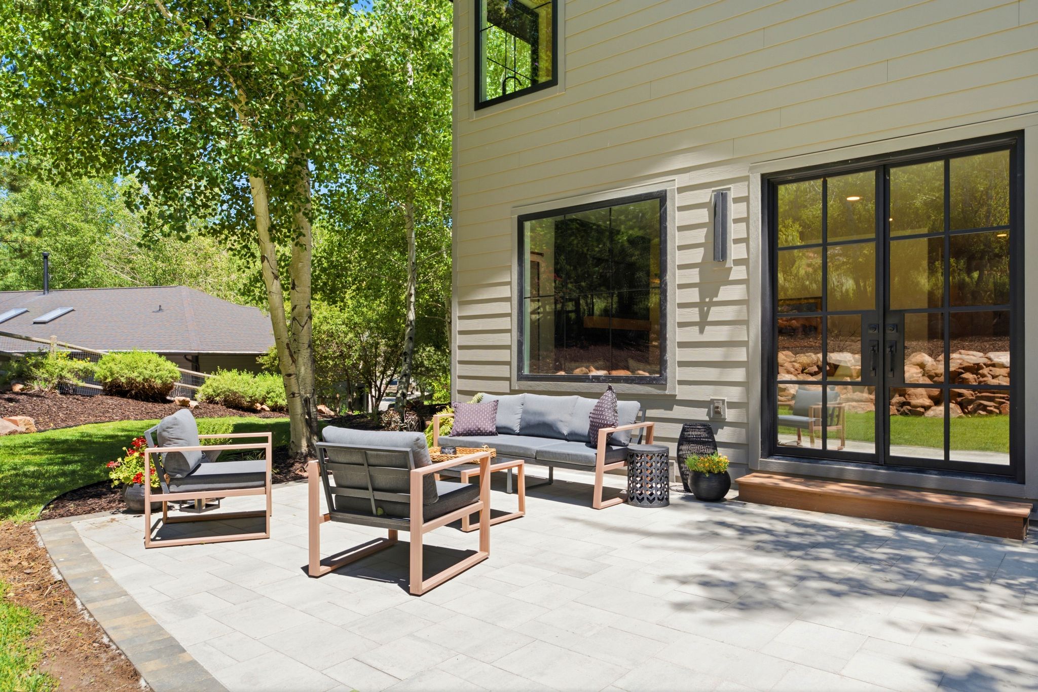 Expansive paver patio with a wood-tone step, black-grid glass doors, and horizontal siding