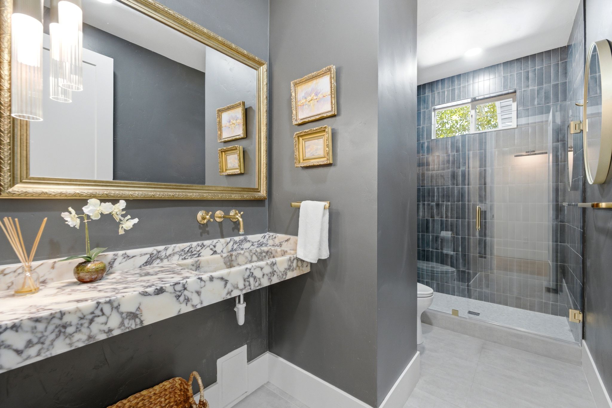Bathroom featuring a floating marble vanity with integrated sink, brass fixtures, a large framed mirror, and a glass-enclosed shower with tiled walls
