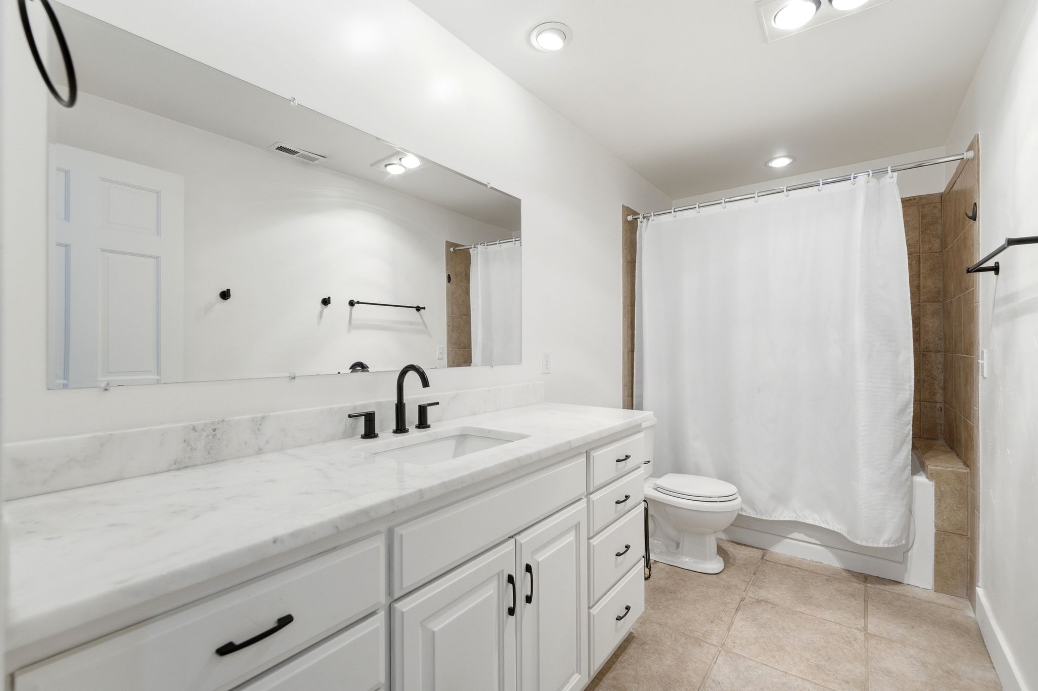 Contemporary bathroom featuring a white vanity with integrated sink, black fixtures, and a large mirror