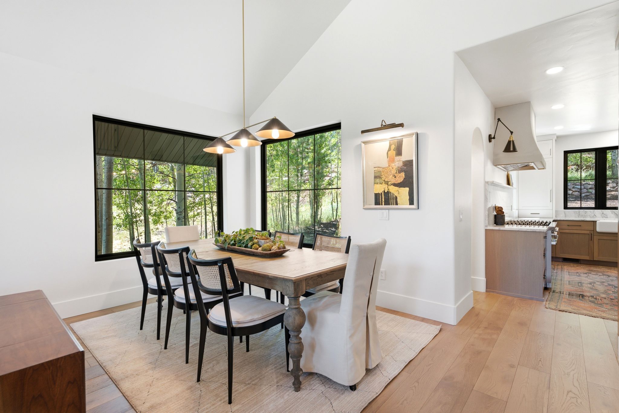 Dining area featuring expansive black-framed windows, vaulted ceilings, wood-finish flooring, and a modern linear chandelier