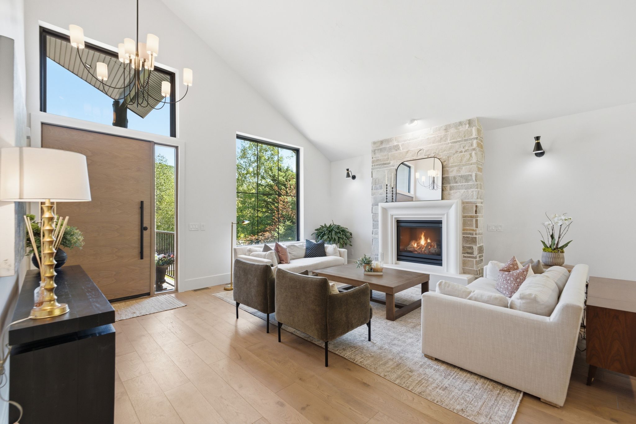 Vaulted ceiling living space featuring a stone fireplace with a white mantel, hardwood flooring, and a large front door with sidelight and transom windows