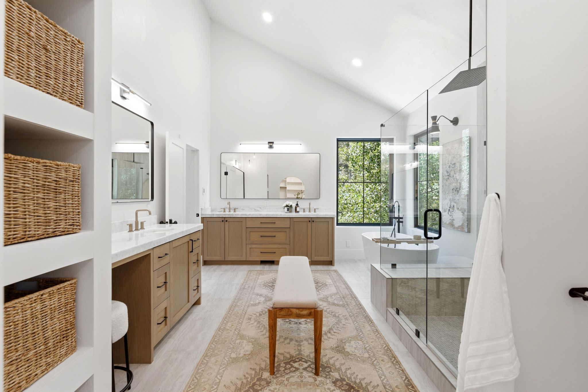 Vaulted ceiling bathroom featuring dual vanities with light wood cabinetry and white countertops