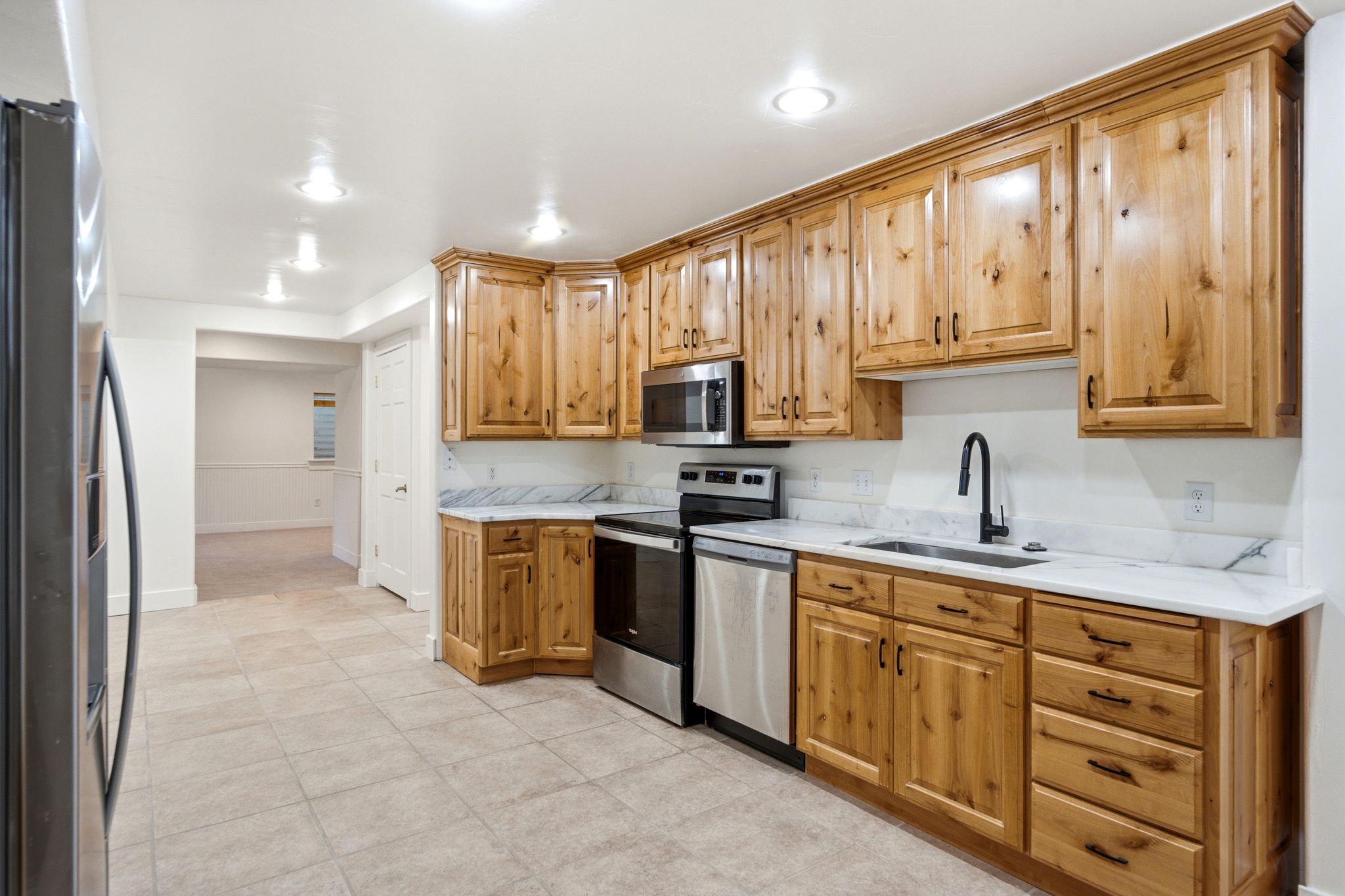 Spacious kitchen featuring natural wood cabinetry, stainless steel appliances, a matte black faucet, white countertops, and tile flooring