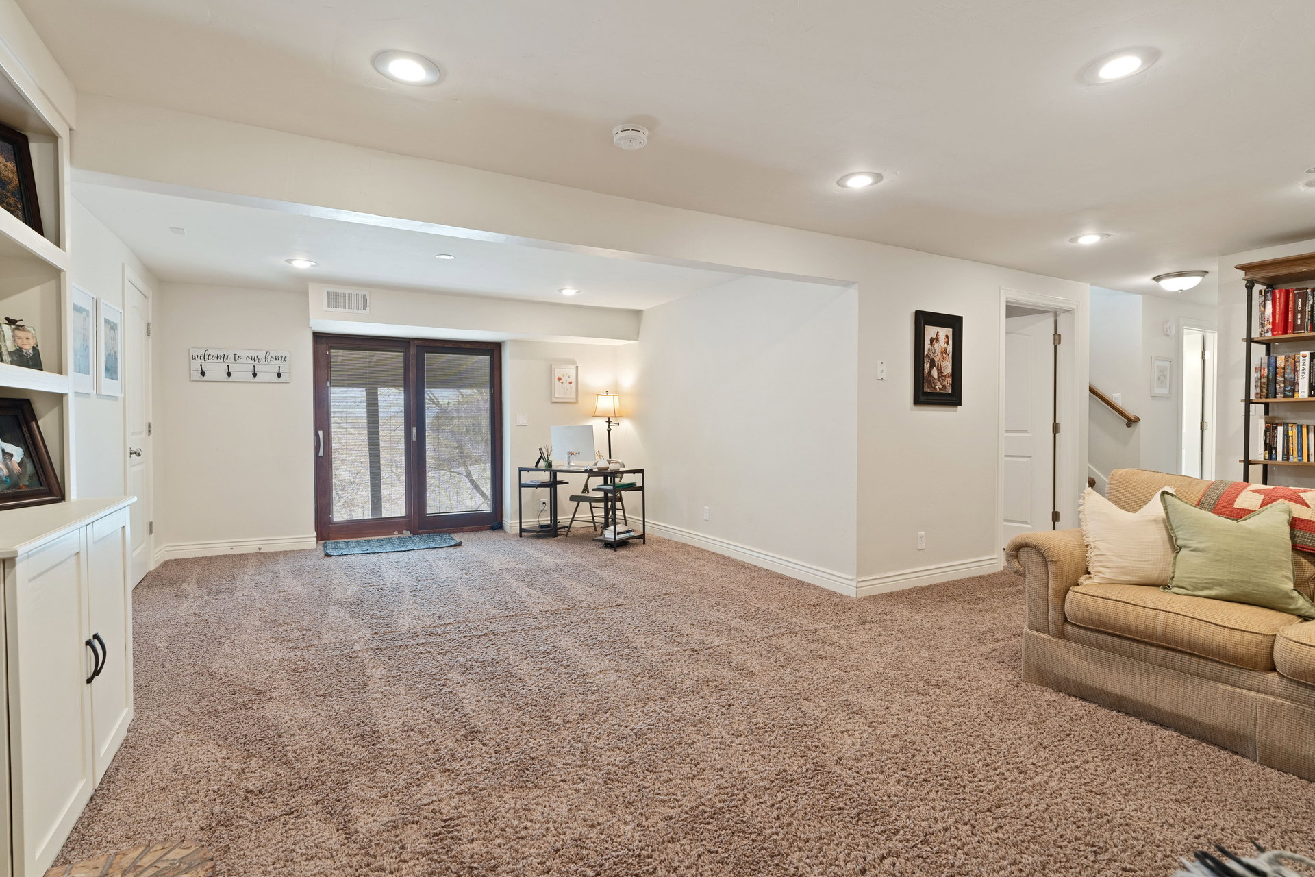 Spacious room featuring plush carpeting, recessed lighting, and a built-in shelving unit with cabinet storage