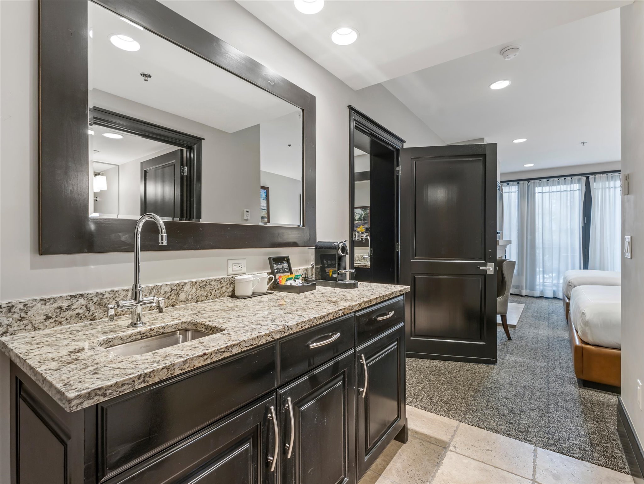 Wet bar featuring a dark wood base cabinet with silver hardware, speckled granite-style countertop, and an undermount stainless steel sink with a chrome faucet