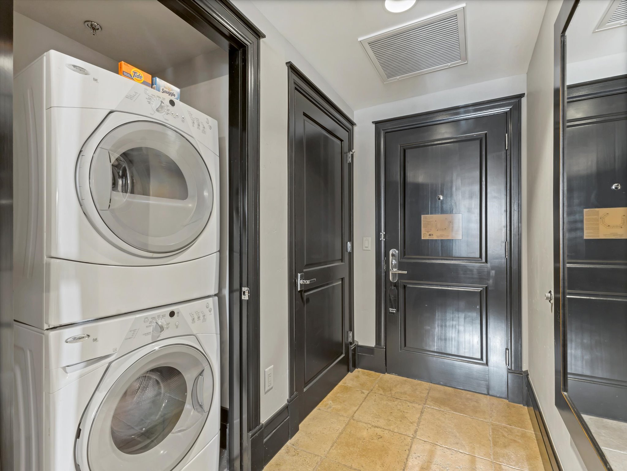 Entryway featuring a stackable washer and dryer, dark-paneled doors, and square tile flooring
