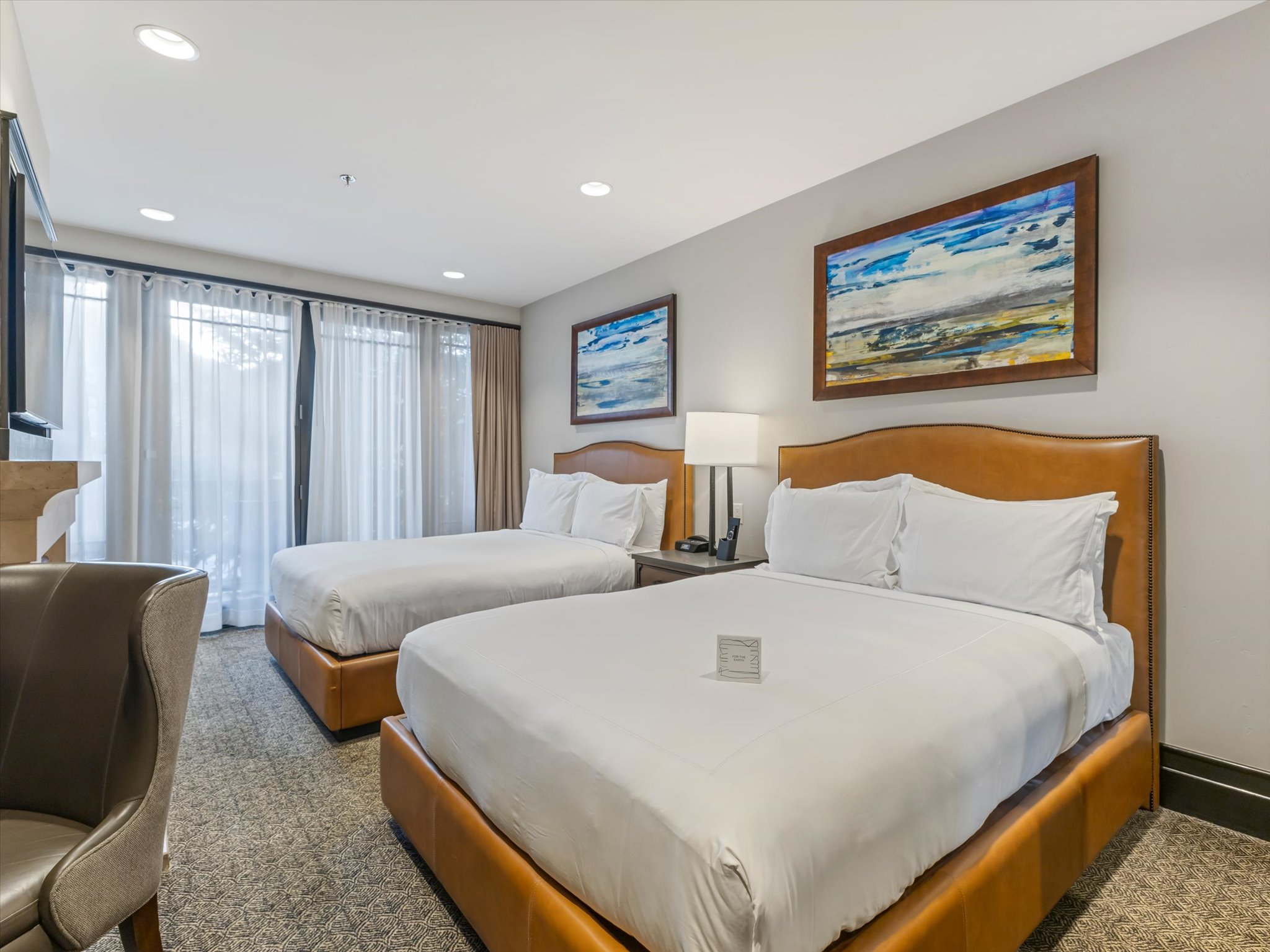 Spacious room with dual beds featuring upholstered headboards, recessed lighting, and direct access to an outdoor area through glass panel doors