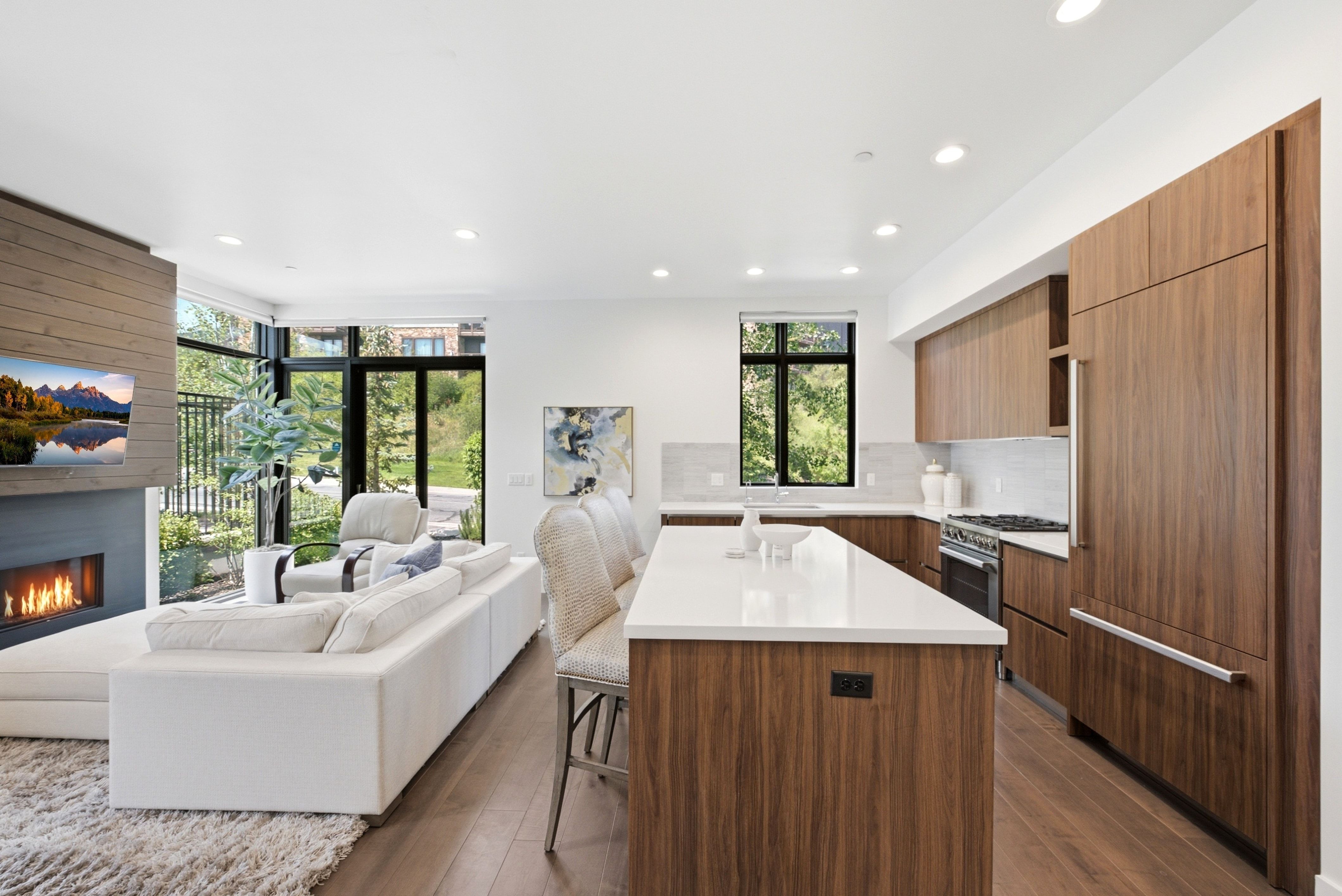 Open-concept living space featuring wood-finish flooring, a modern fireplace with a wood-paneled accent, and expansive windows