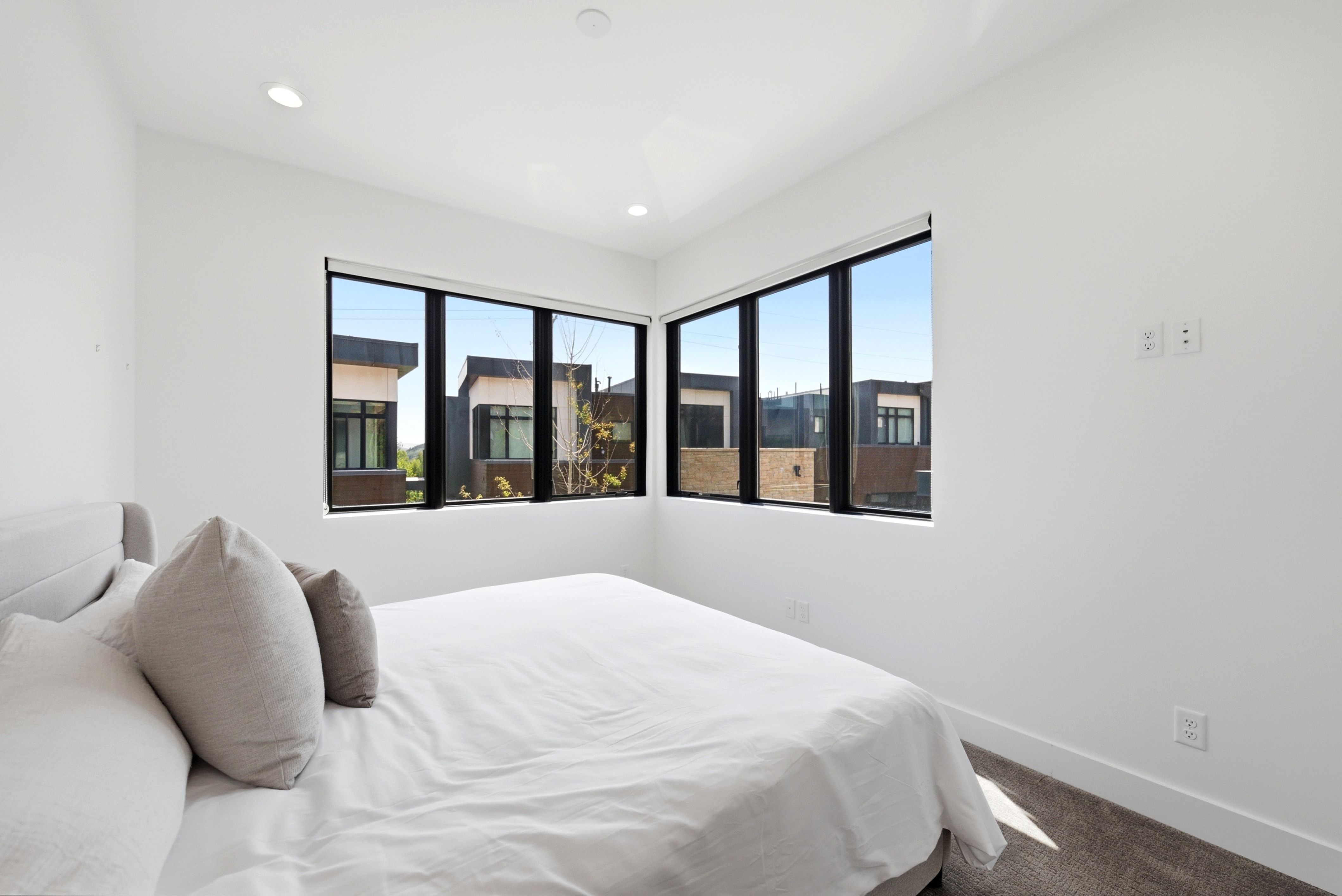 Bedroom featuring expansive black-framed windows, recessed lighting, white walls, and gray carpet flooring