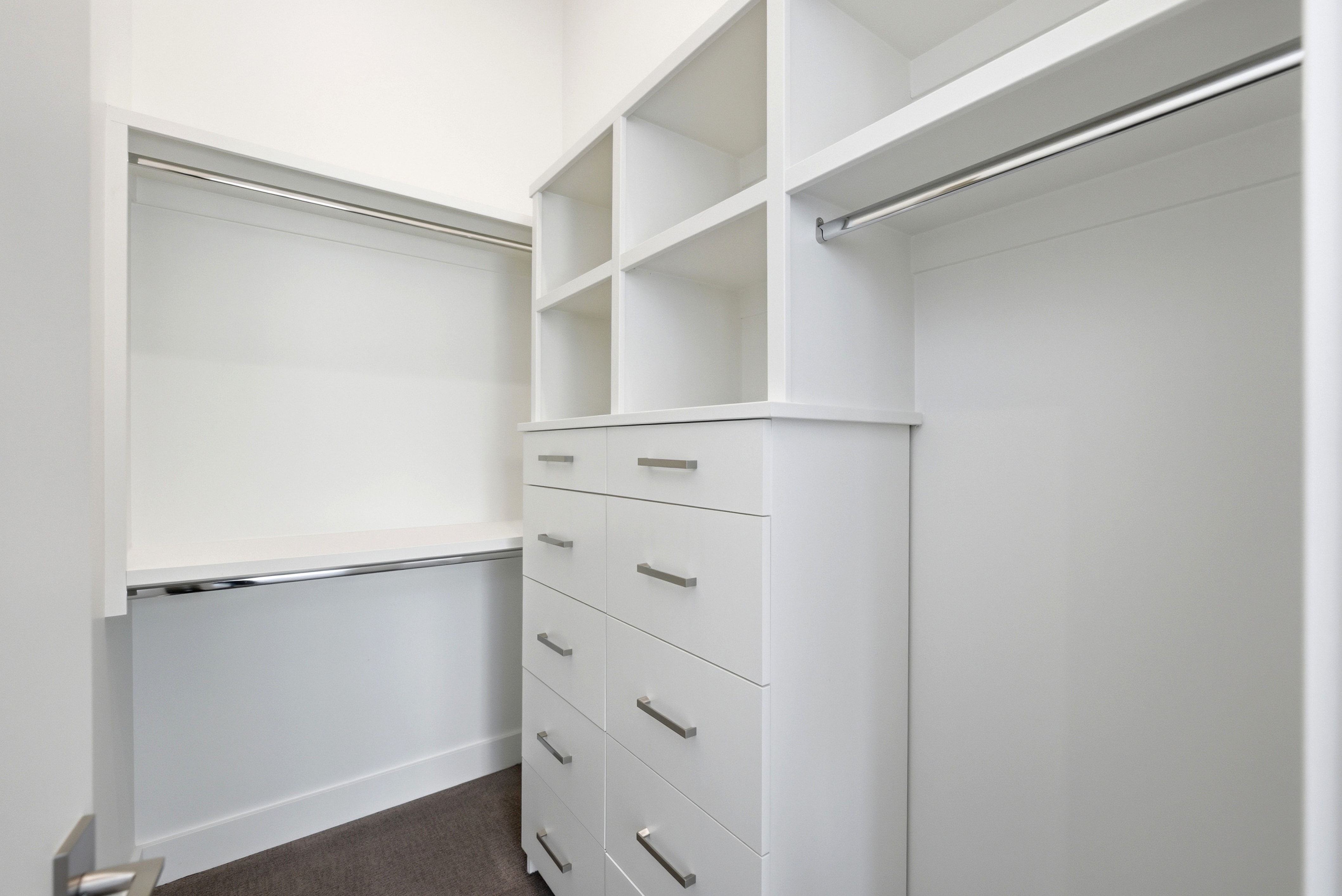 Walk-in closet featuring white built-in cabinetry, shelving, multiple hanging rods, and drawers with brushed nickel pulls
