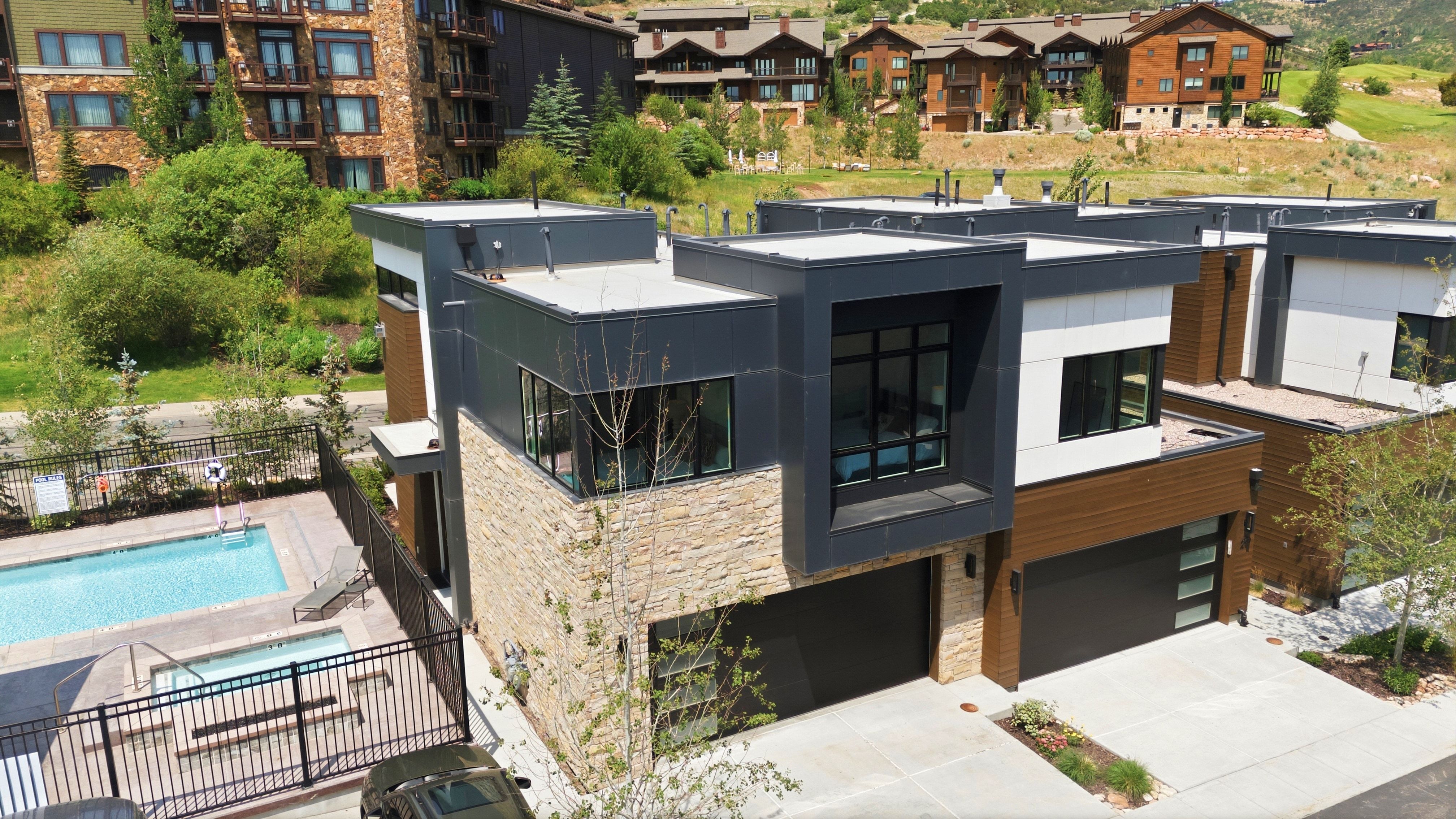 Modern architectural residence featuring a stone and dark panel facade, a flat roofline, and integrated garage doors
