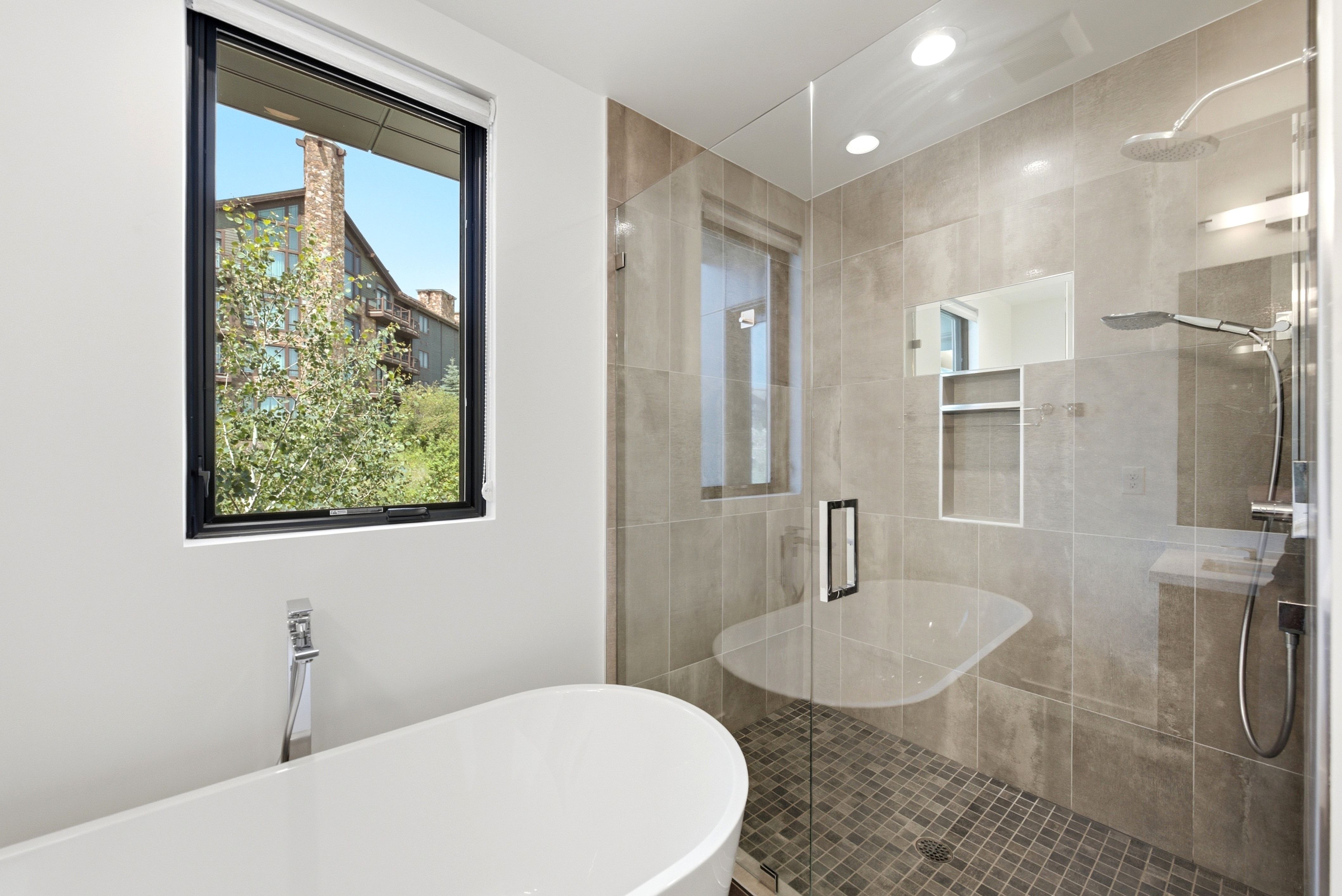 Contemporary bathroom featuring a freestanding soaking tub with a floor-mounted faucet, a spacious walk-in shower with large format wall tiles, a mosaic tile shower floor, and a built-in shower bench