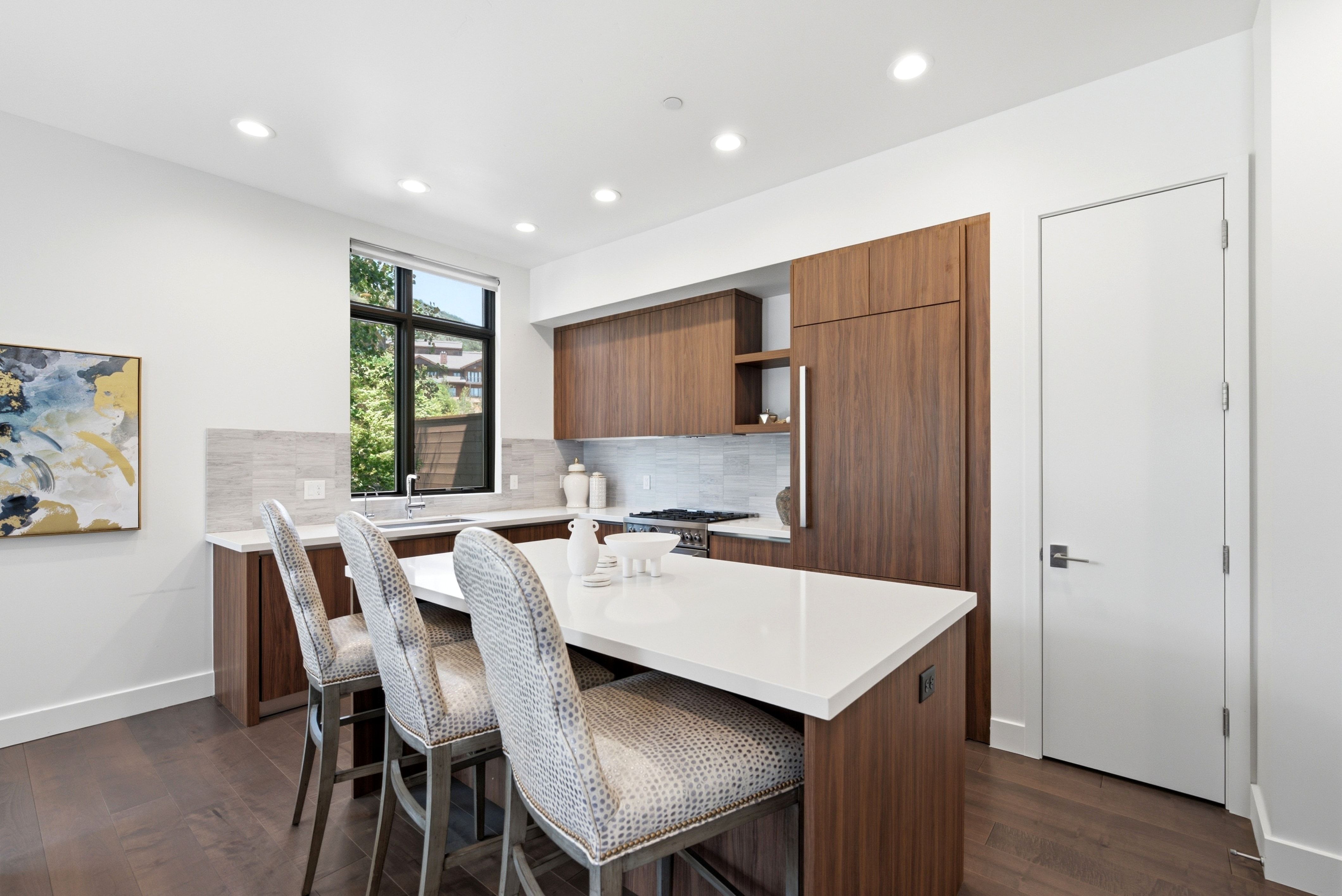 Modern kitchen featuring a central island with a white countertop, recessed lighting, wood-finish flooring, and integrated wood-panel appliances