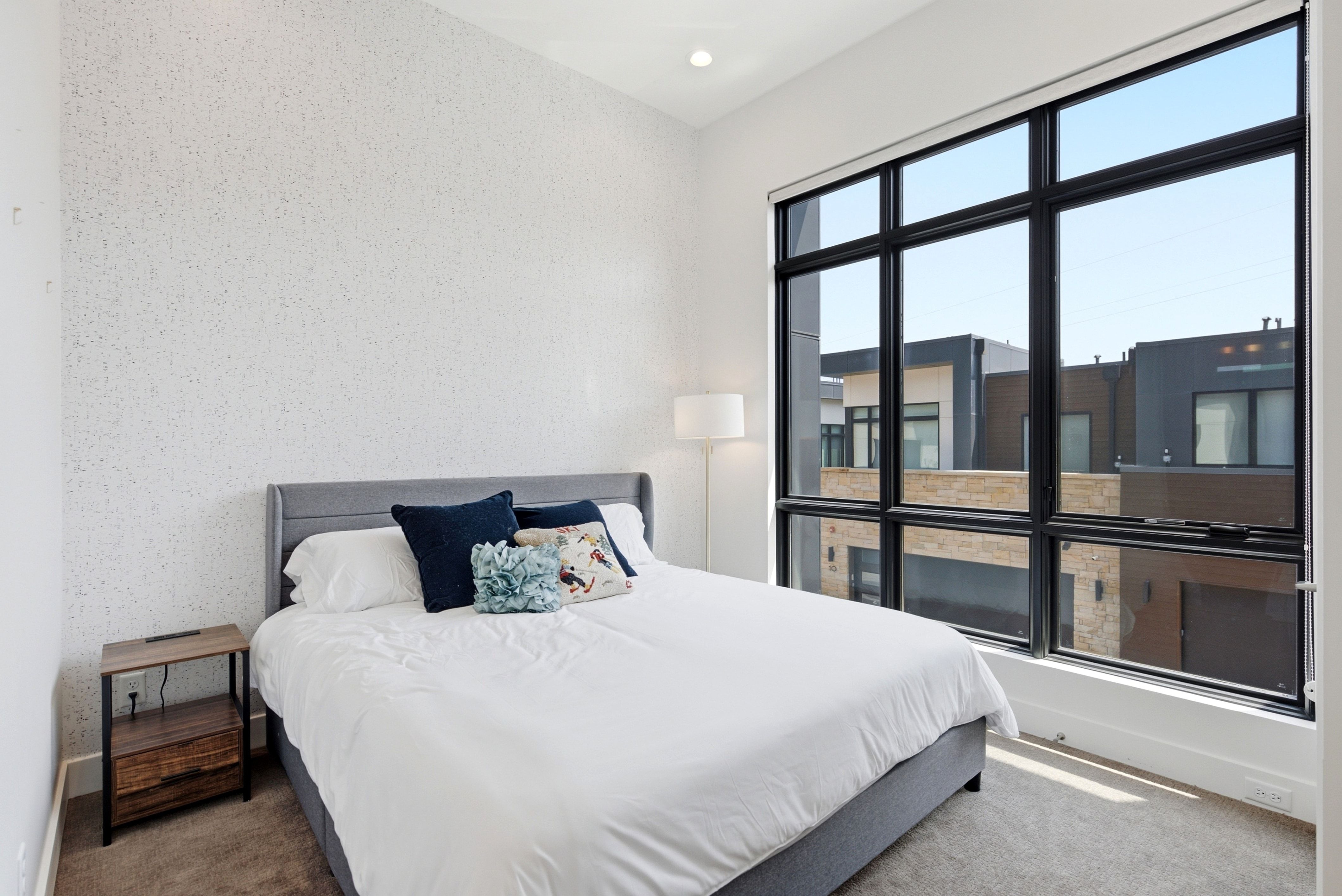 Full-height multi-pane window with black framing, white textured accent wall, recessed lighting, and carpeted flooring