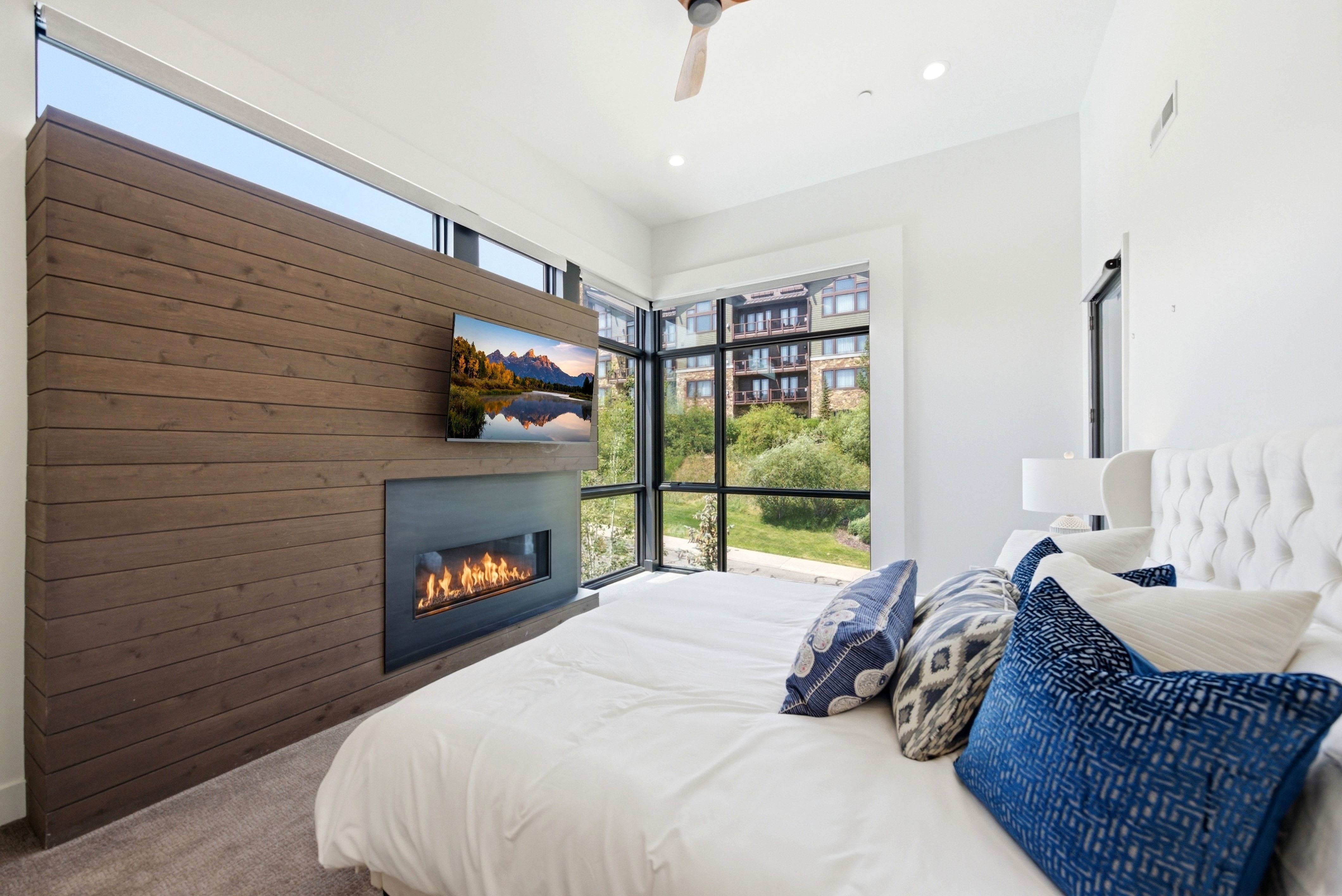 Contemporary bedroom featuring a linear fireplace with a dark metal surround, a wood-paneled accent wall, and expansive multi-pane windows