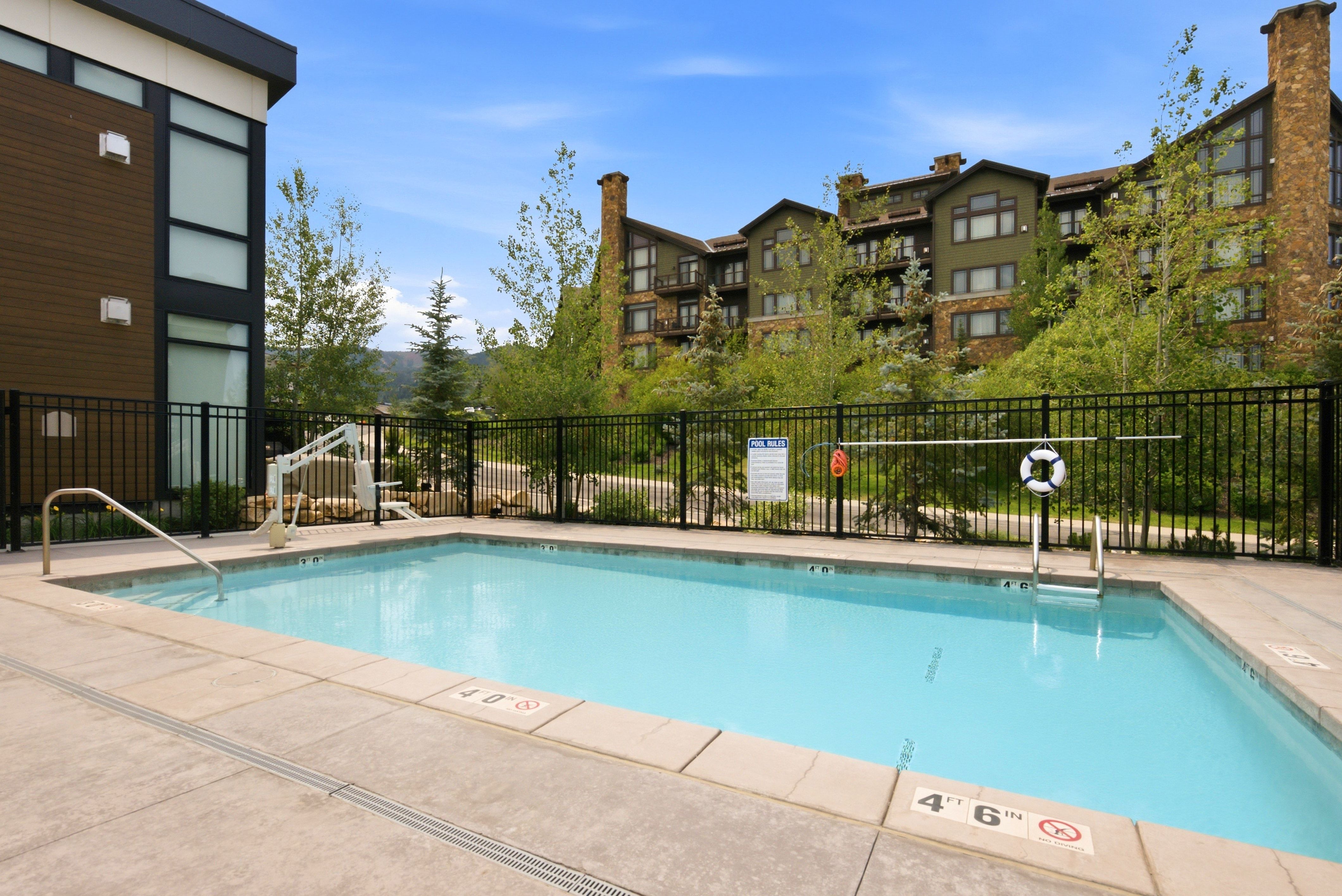 Outdoor swimming pool with integrated accessibility lift, surrounded by concrete decking and a black metal fence