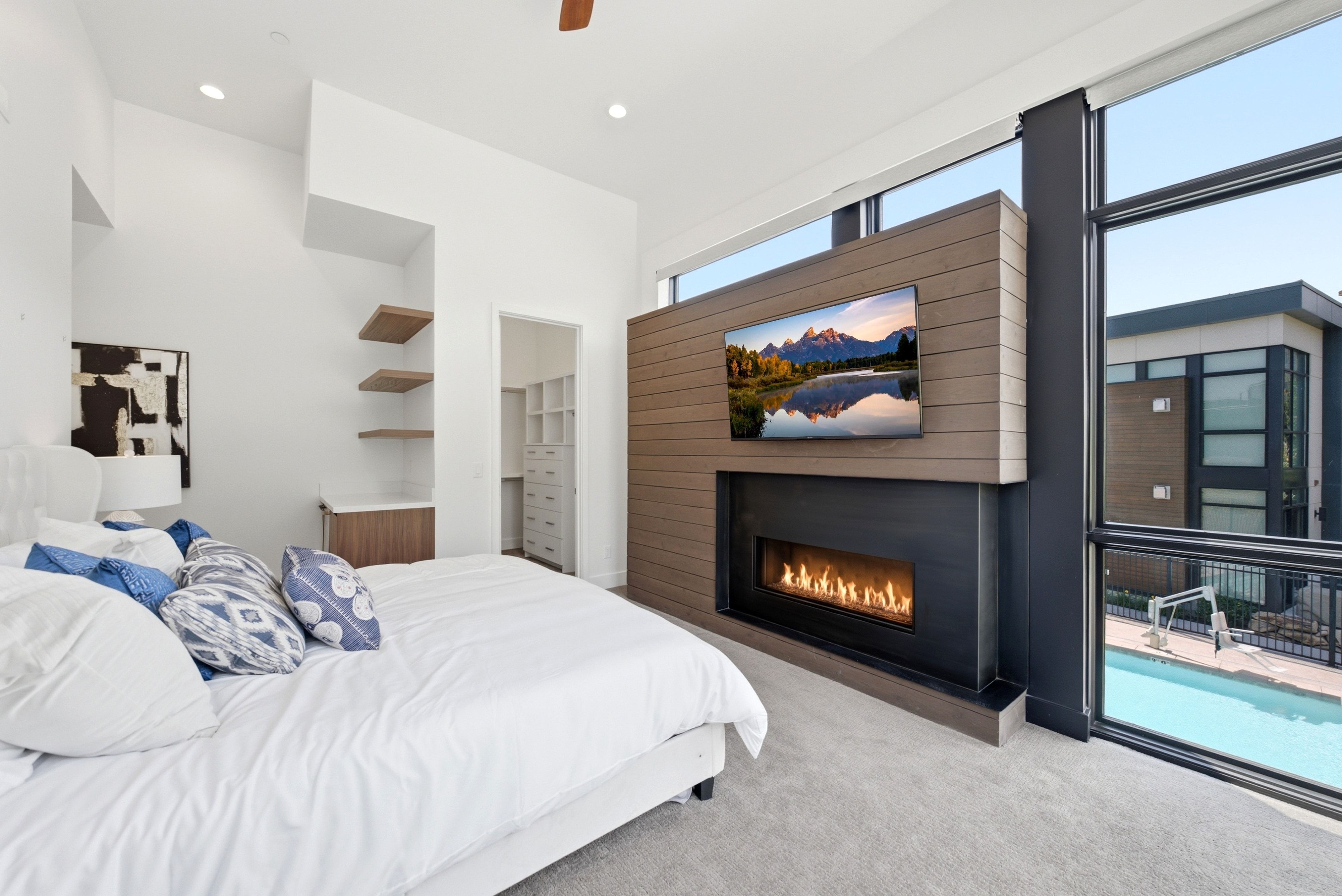 Carpeted room featuring a modern linear fireplace with wood-finish paneling, floor-to-ceiling windows, and a walk-in closet with built-in shelving