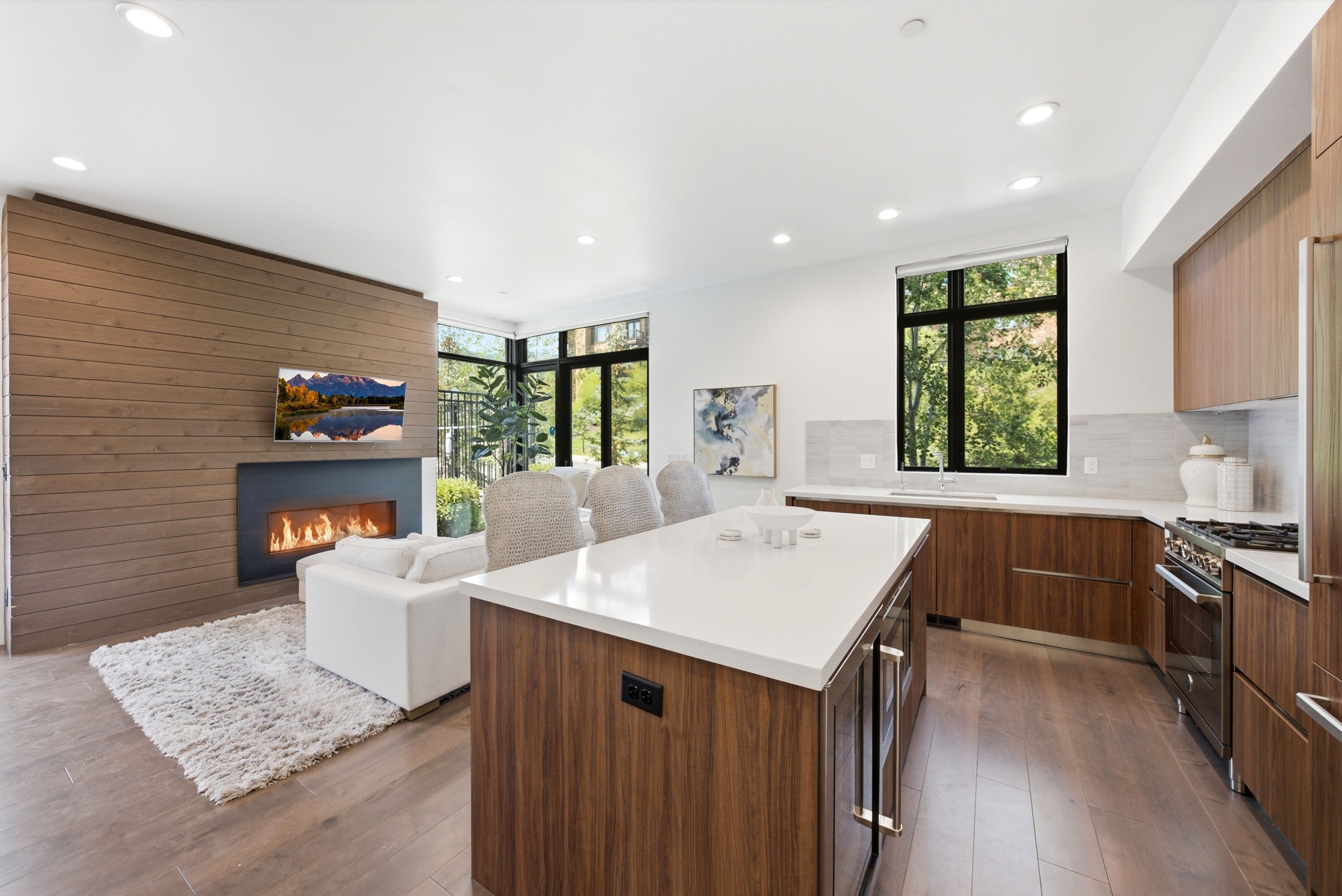 Open-concept living space featuring wood-finish flooring, a contemporary fireplace with a horizontal firebox, and recessed lighting