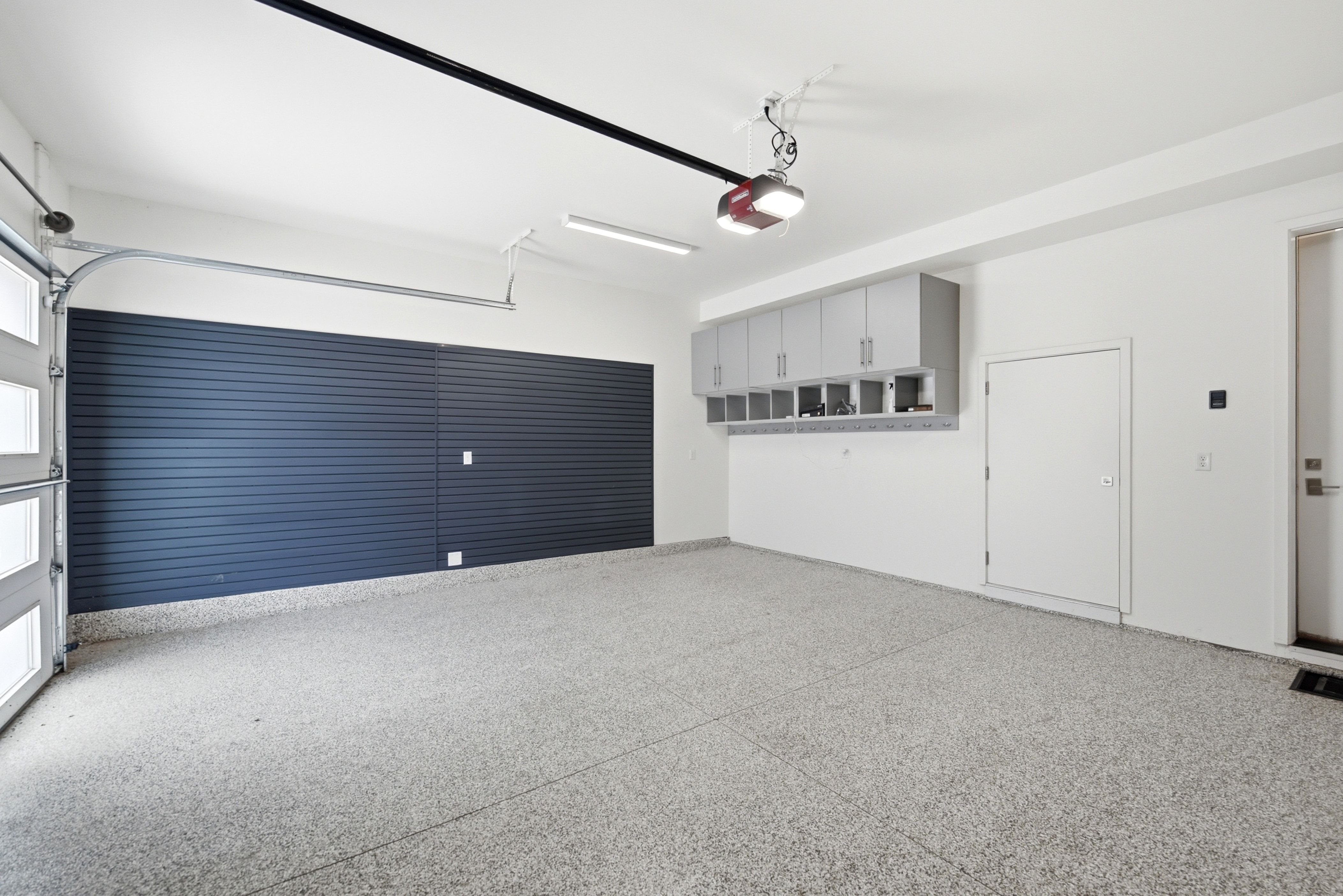 Spacious garage featuring a durable epoxy floor, slatwall storage system, overhead cabinetry, and an automatic garage door opener