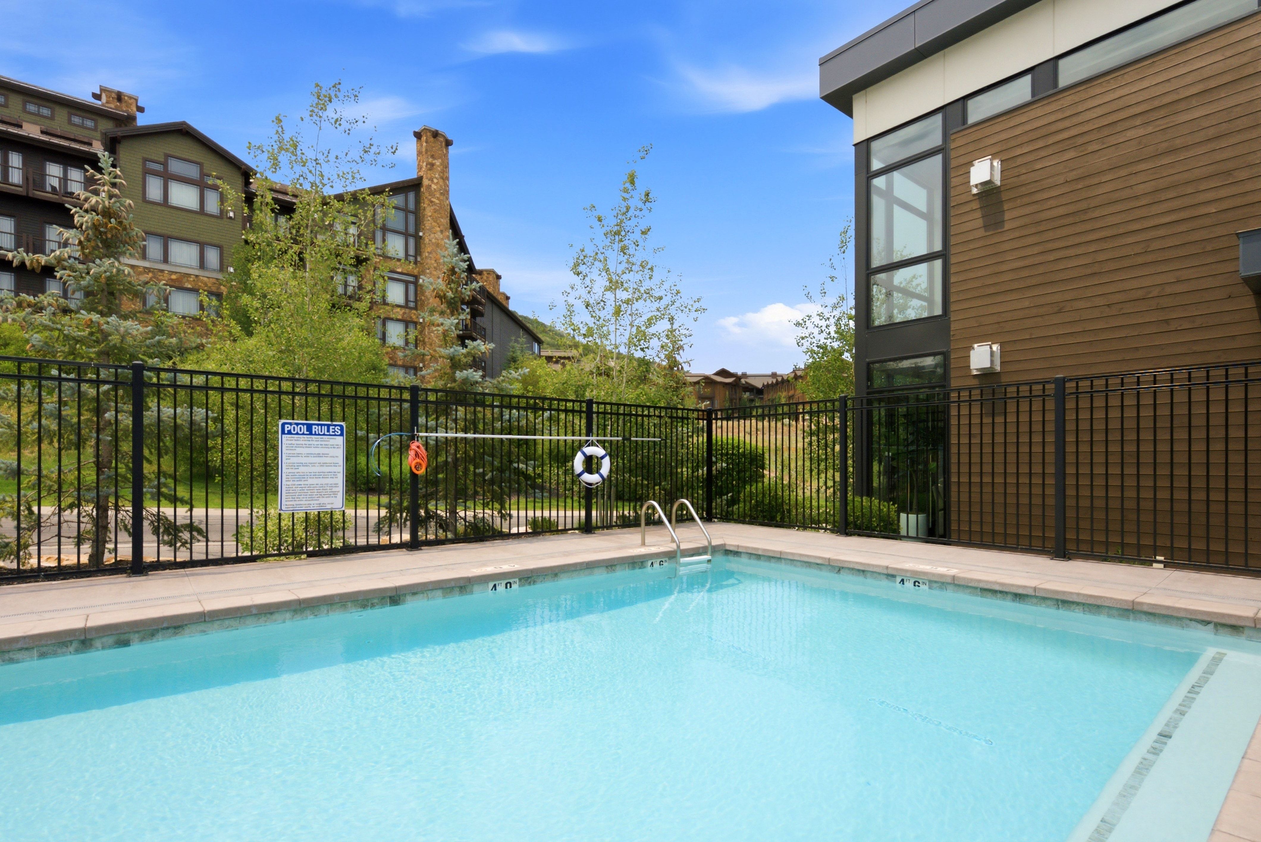Outdoor swimming pool with integrated steps and metal handrails, surrounded by a black metal fence and concrete decking