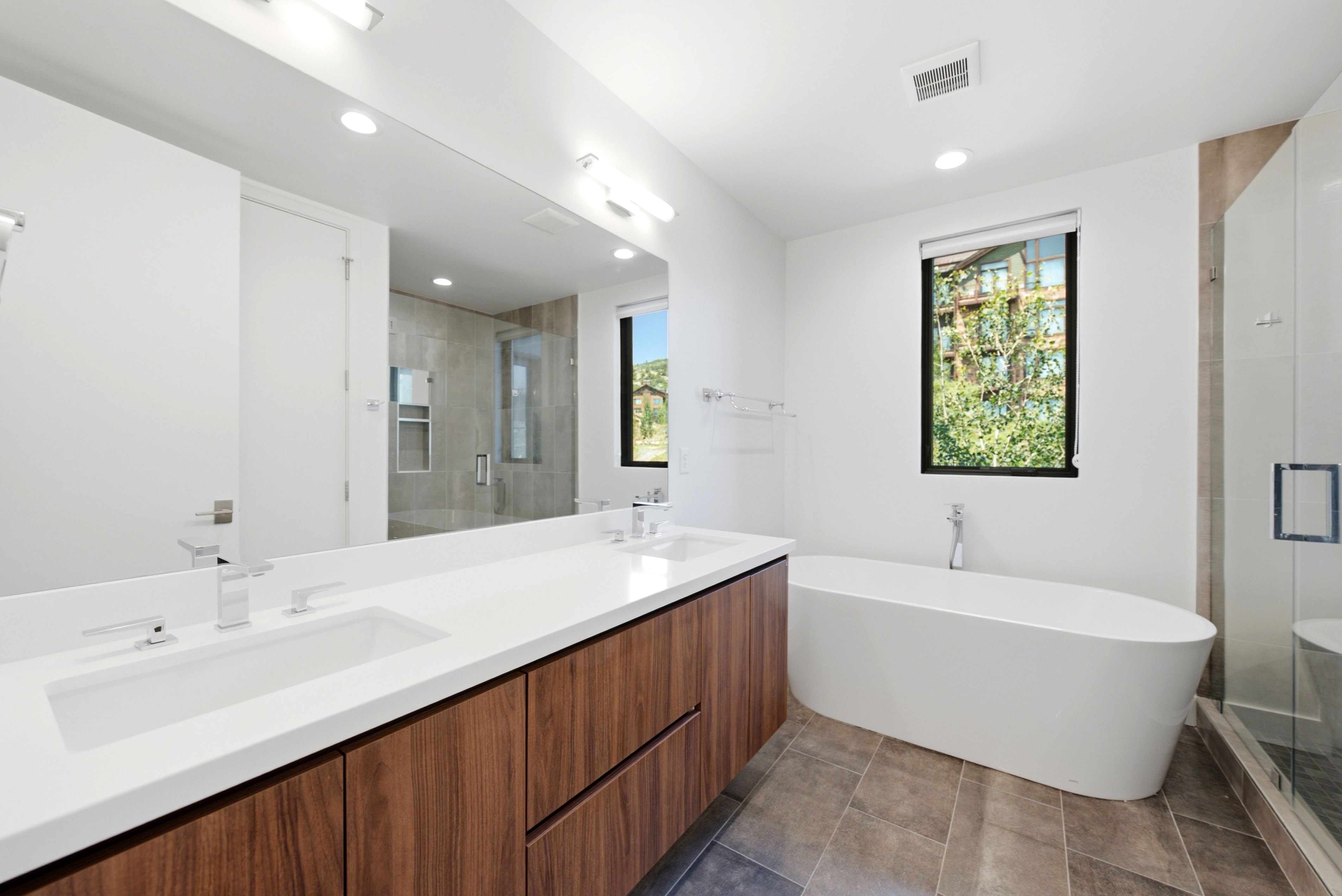 Modern bathroom featuring a wood-finish double vanity with integrated sinks and white countertops, a freestanding soaking tub, a glass-enclosed shower, and tile flooring
