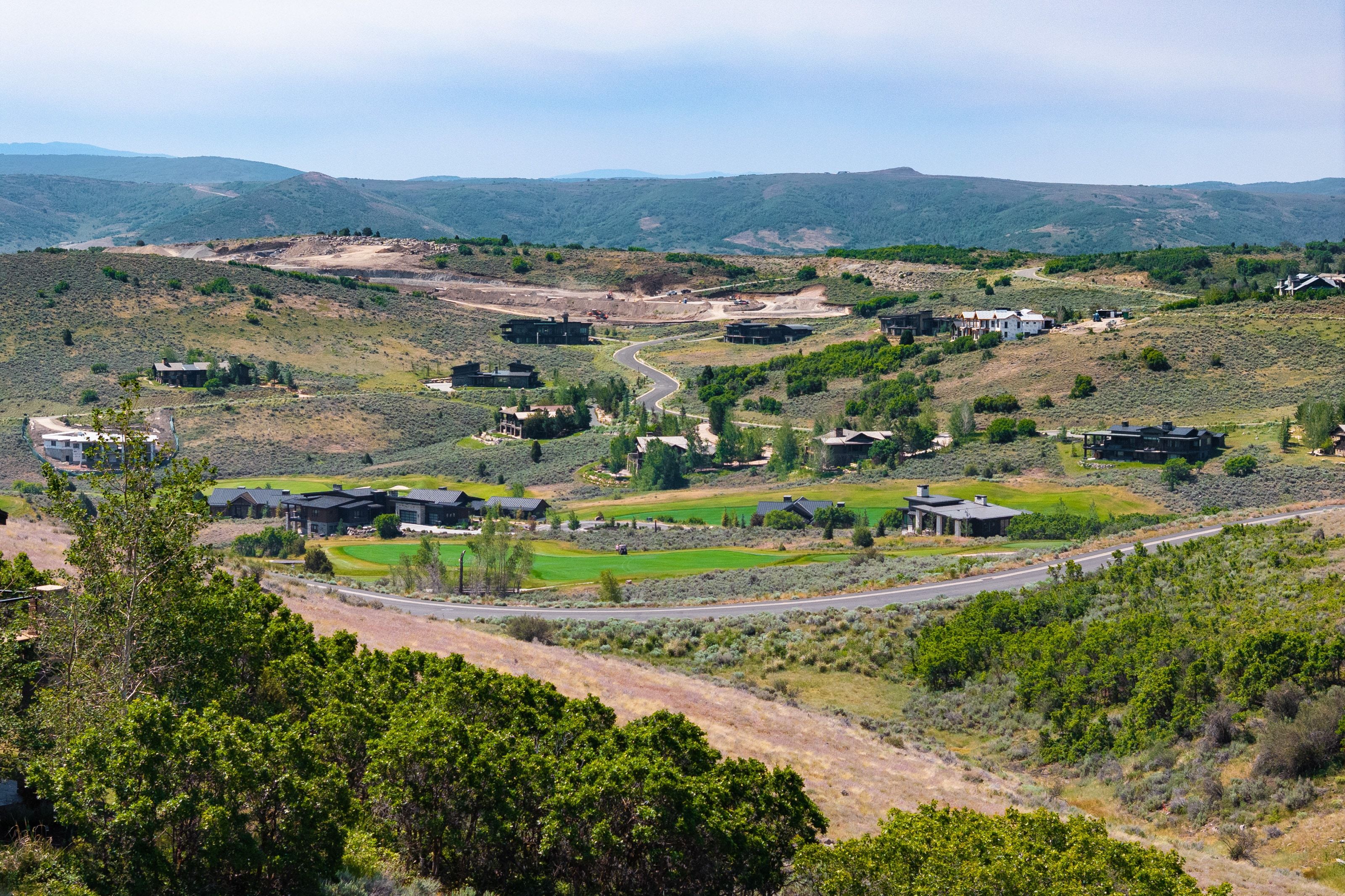 Expansive elevated landscape featuring distant homes, a golf course, paved roads, and rolling hills with natural vegetation