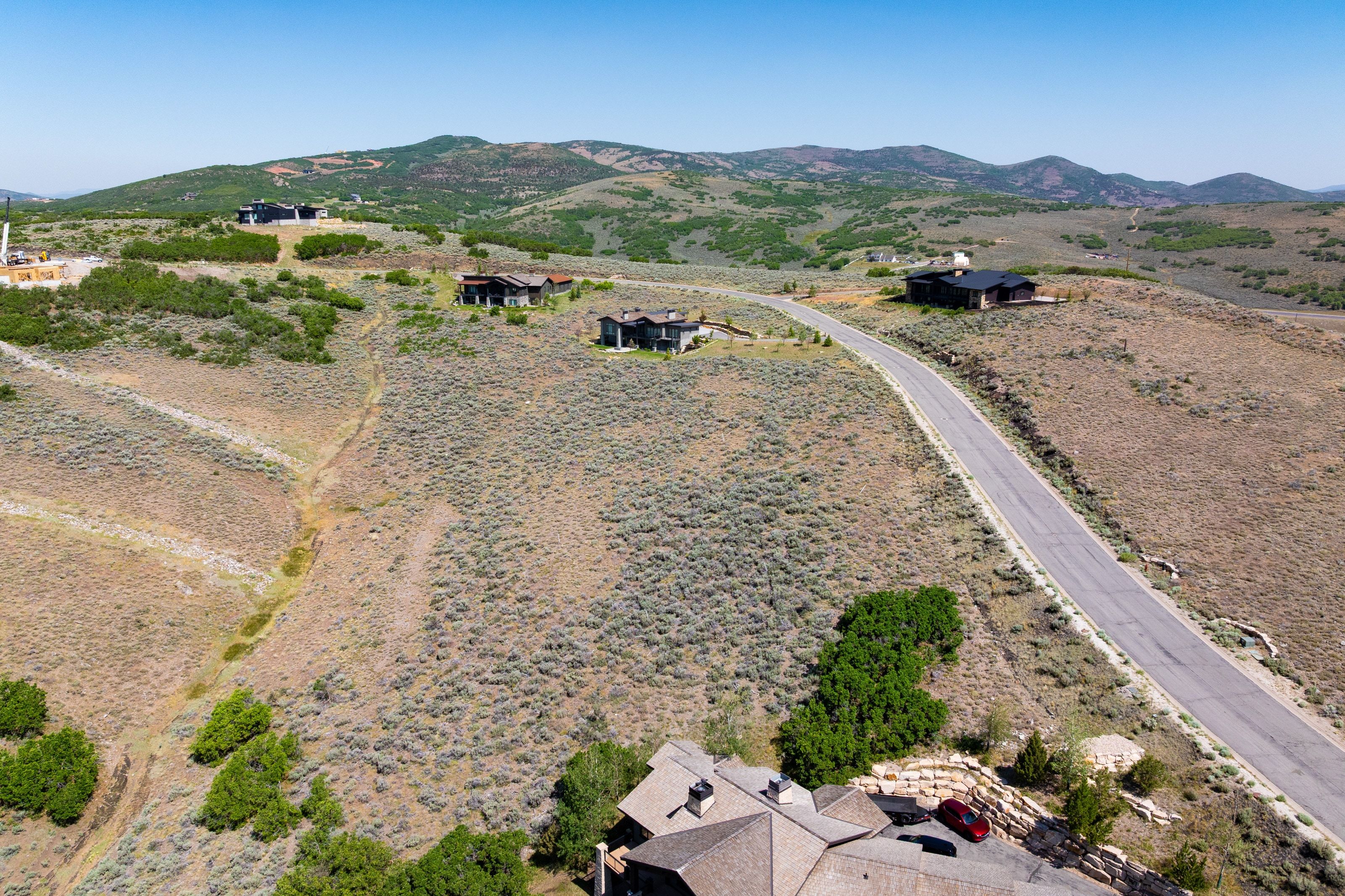 Expansive hillside property featuring a paved road, scattered natural vegetation, and distant mountain topography
