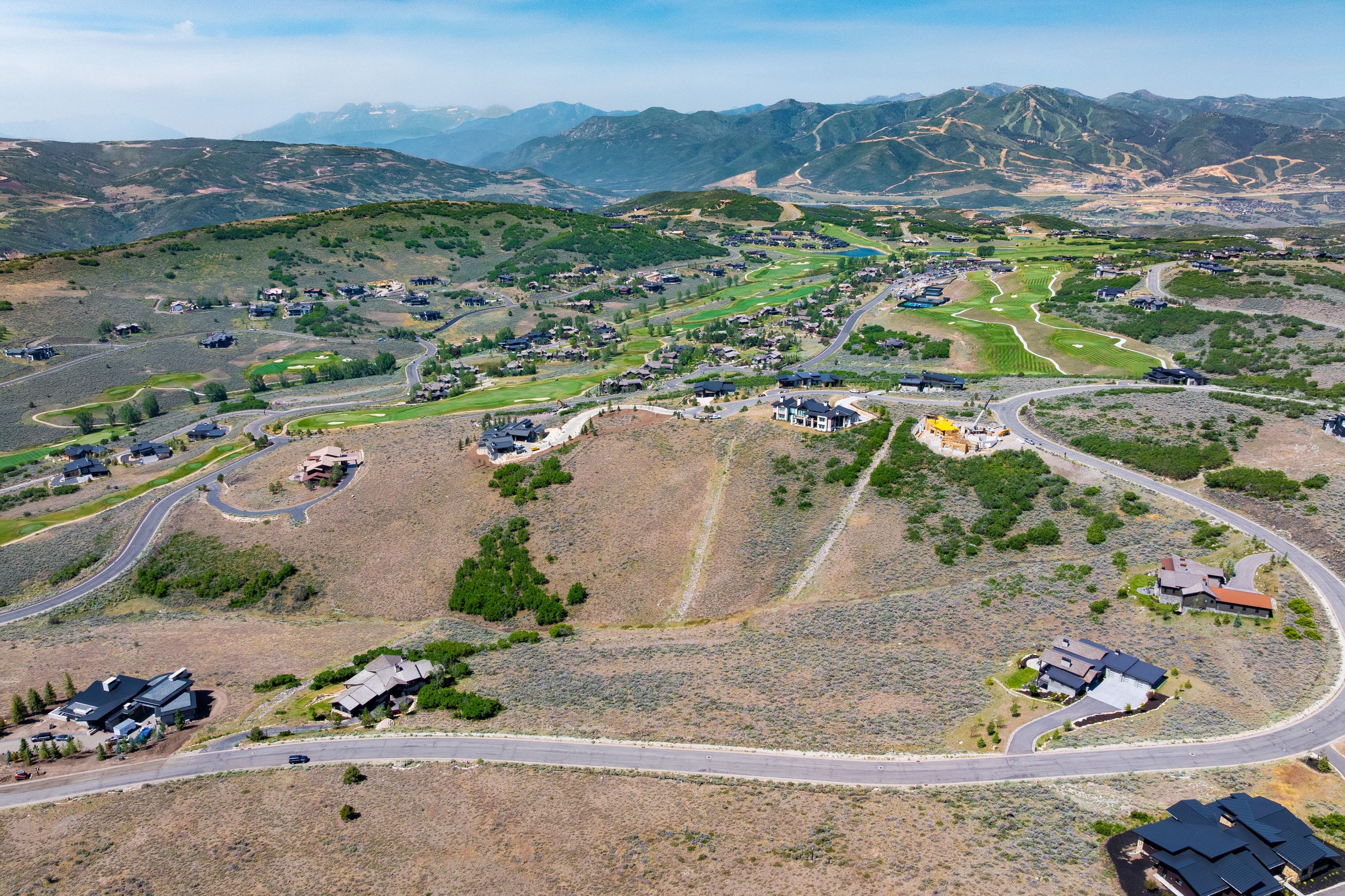 Expansive mountainous terrain featuring scattered residential properties, paved winding roads, and distant golf course greens