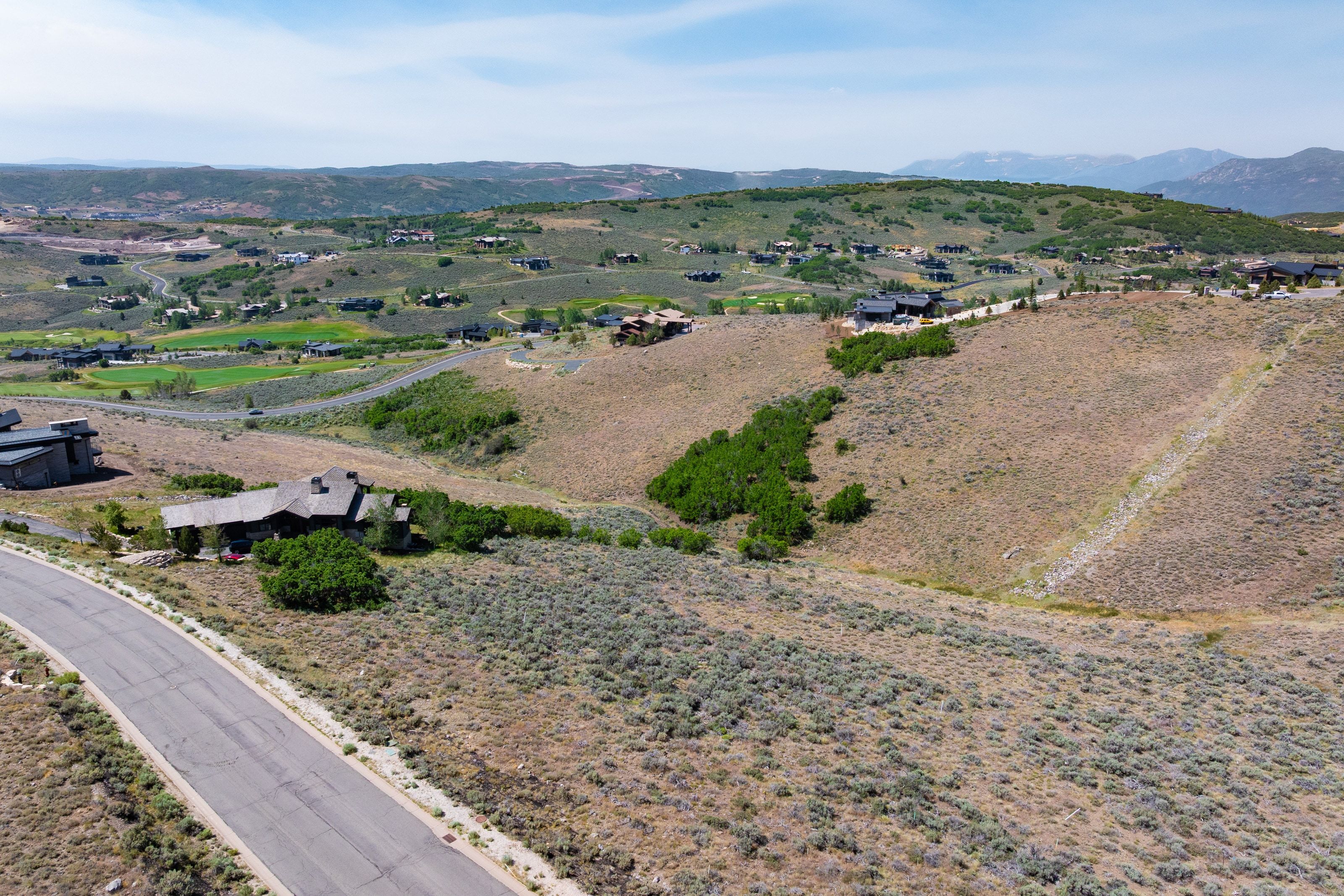 Expansive sloped terrain featuring natural desert vegetation, a paved roadway, and distant residential structures