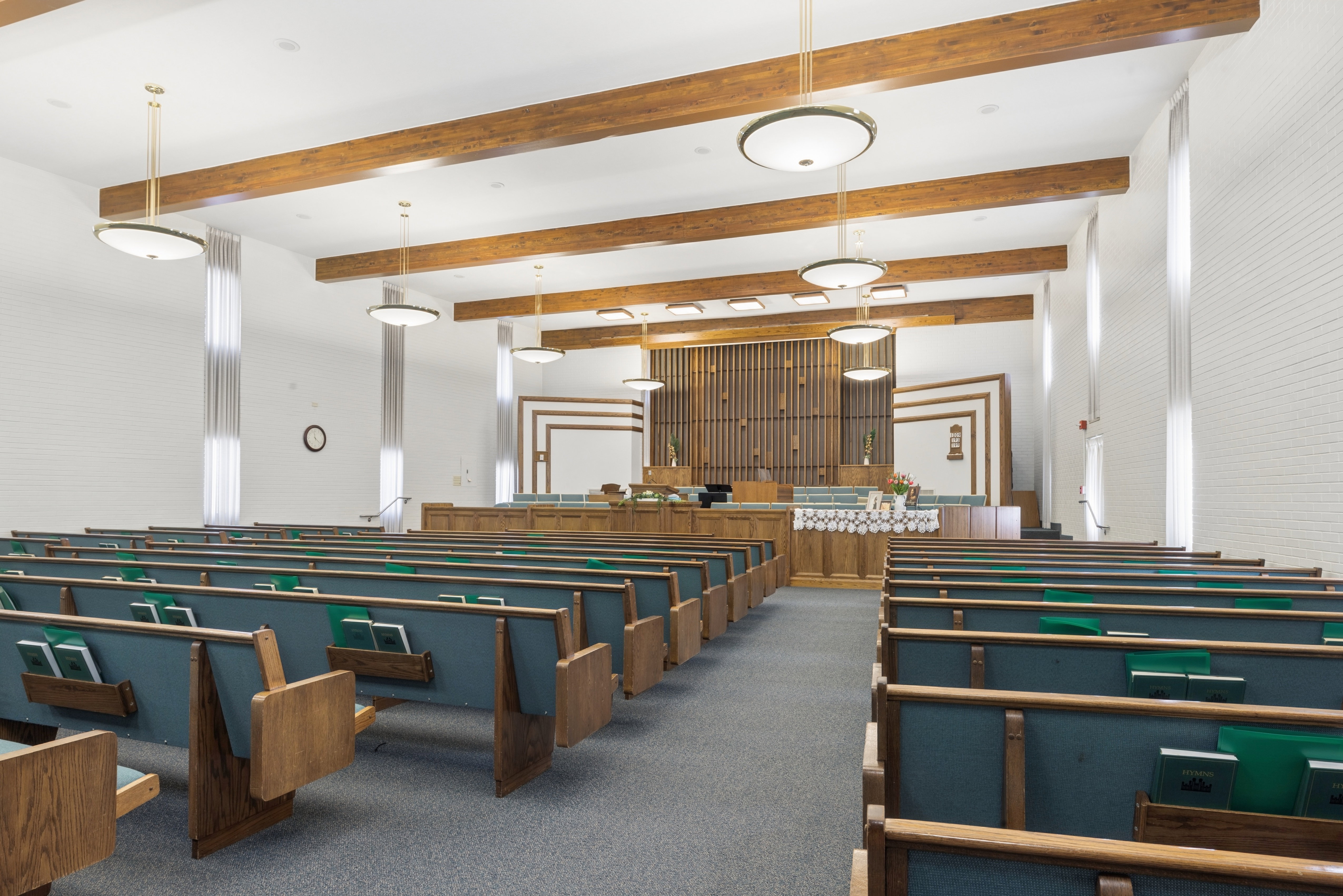 Chapel featuring wood-finish ceiling beams, upholstered wooden pews, and suspended lighting fixtures