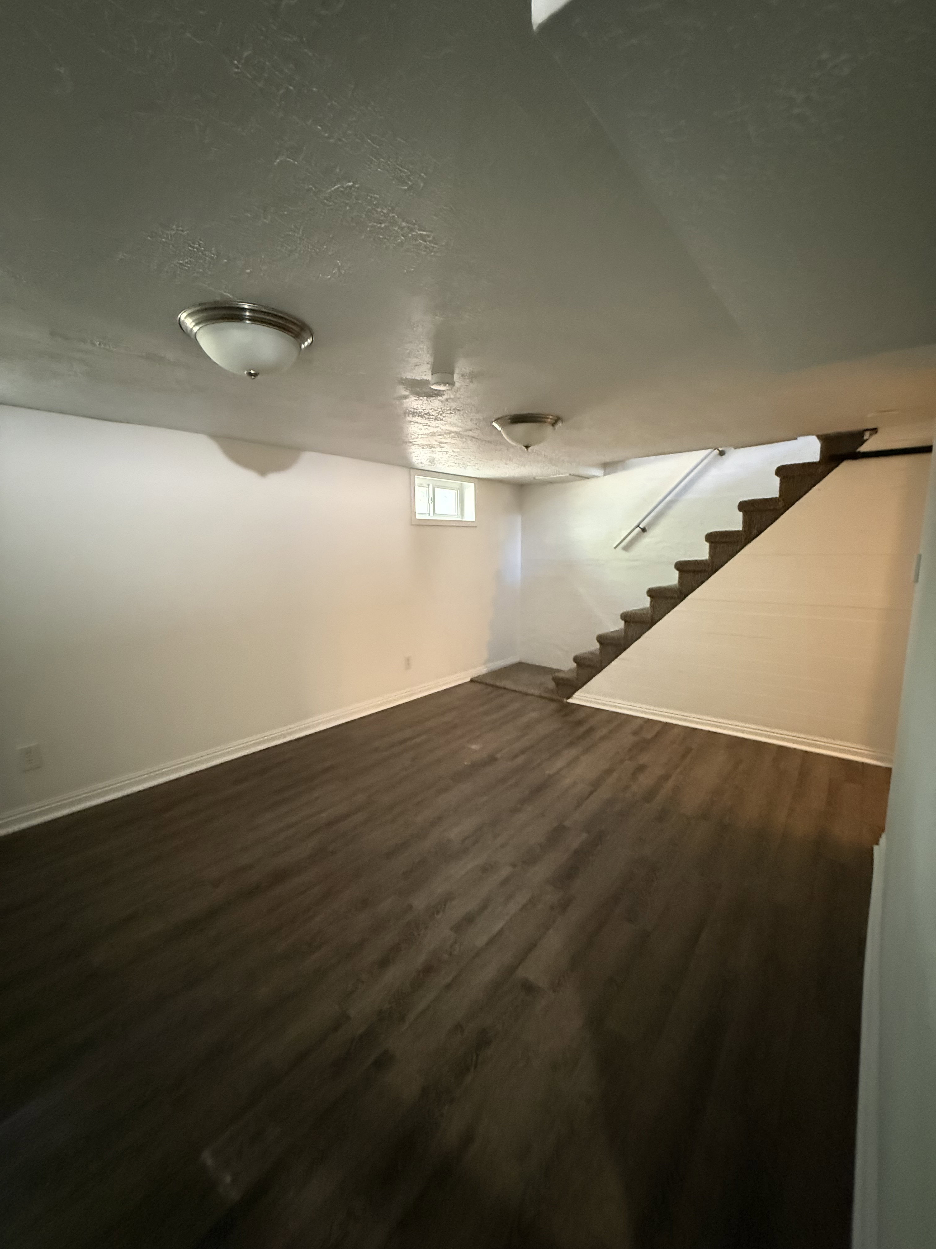 Spacious room featuring wood-finish flooring, white baseboards, and neutral wall tones