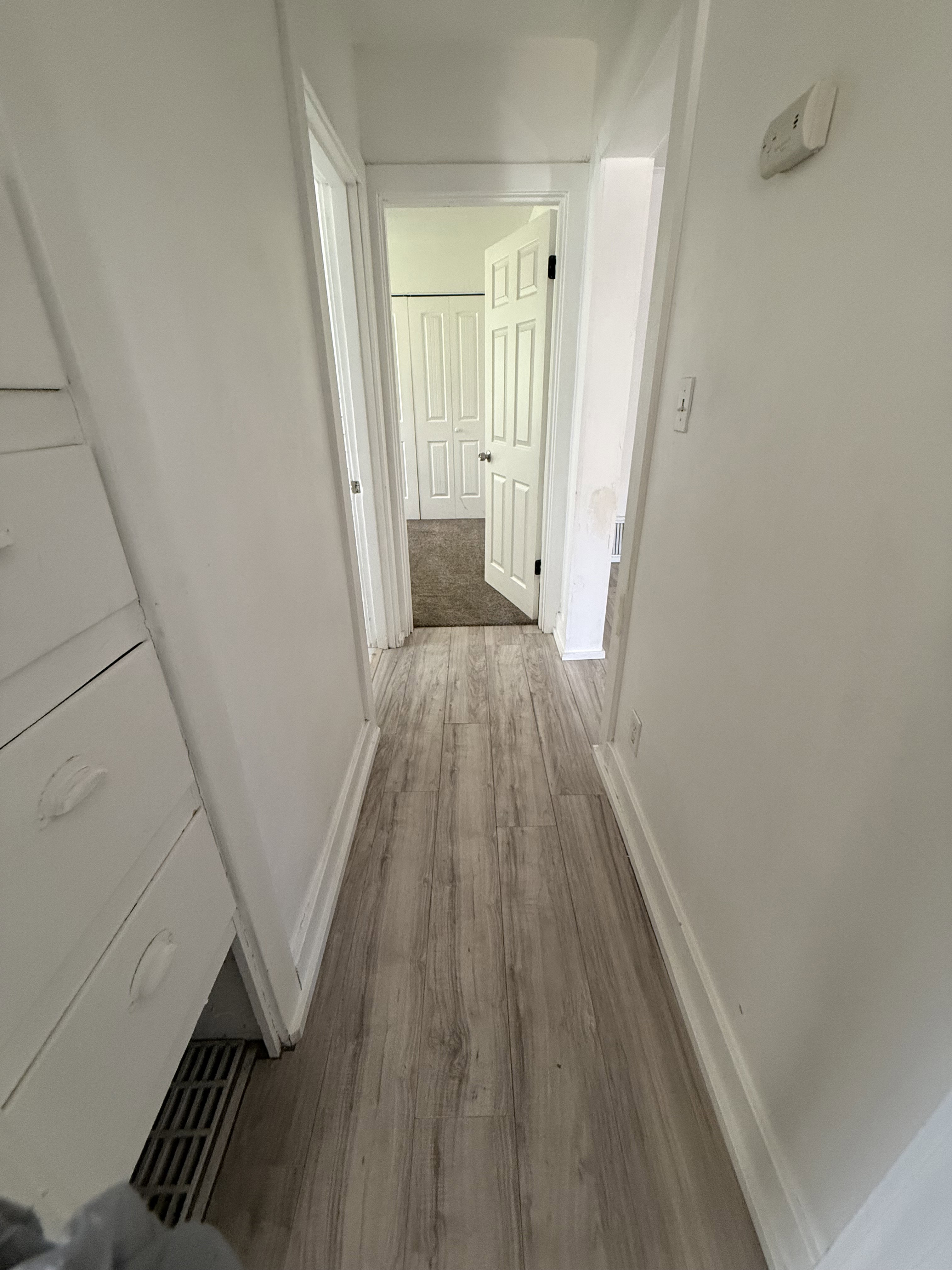 Hallway featuring wood-finish flooring, white baseboards, and white walls