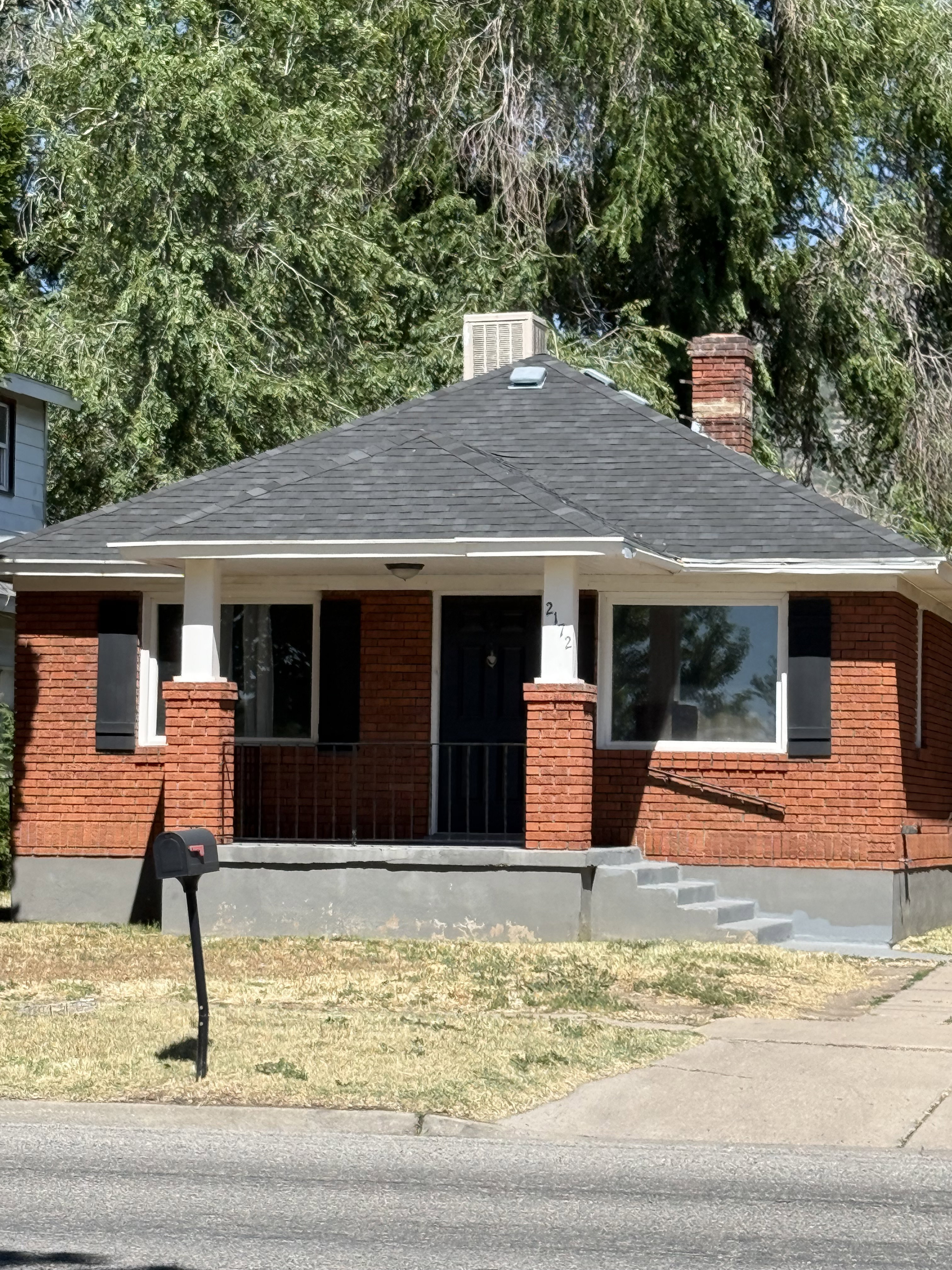Brick facade residence featuring a dark asphalt shingle roof and a front porch with black railings