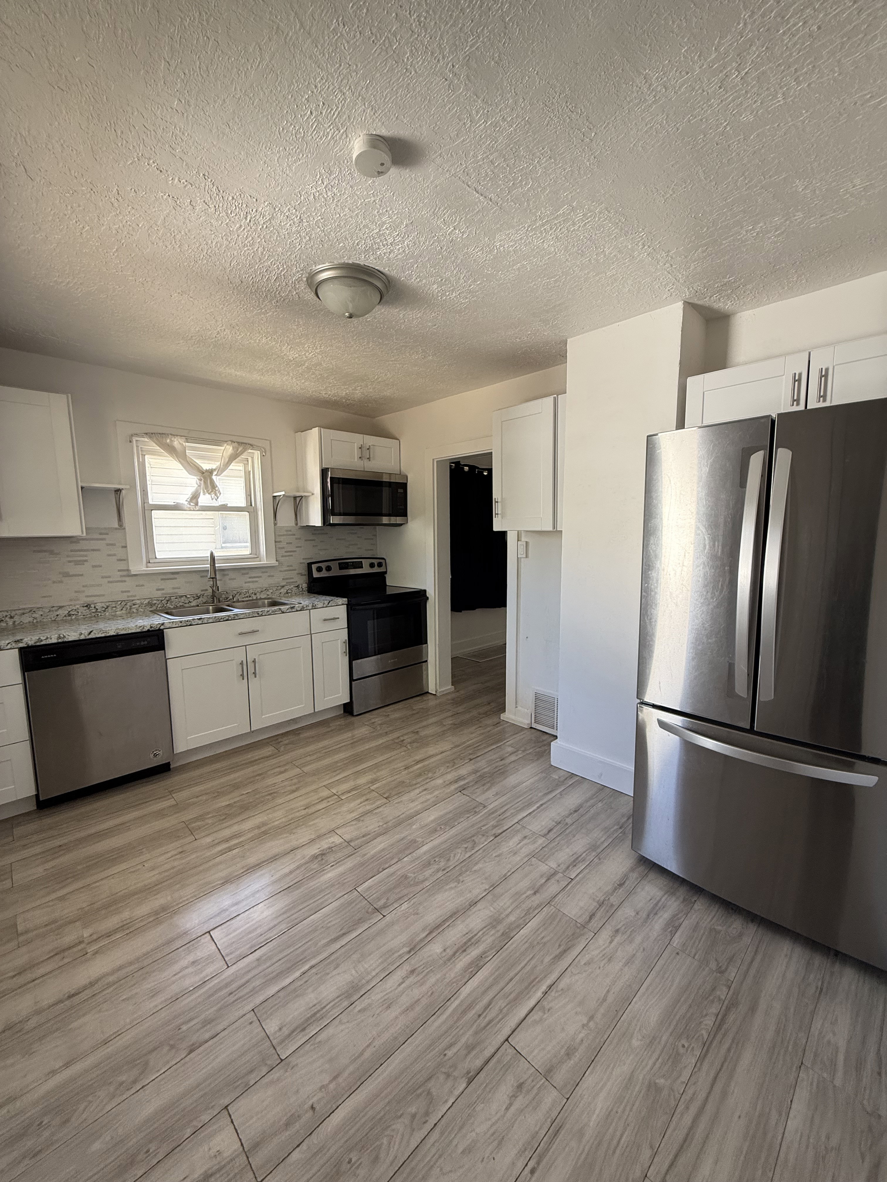 Contemporary kitchen featuring stainless steel appliances, white cabinetry, wood-finish flooring, light-toned countertops, and a tiled backsplash