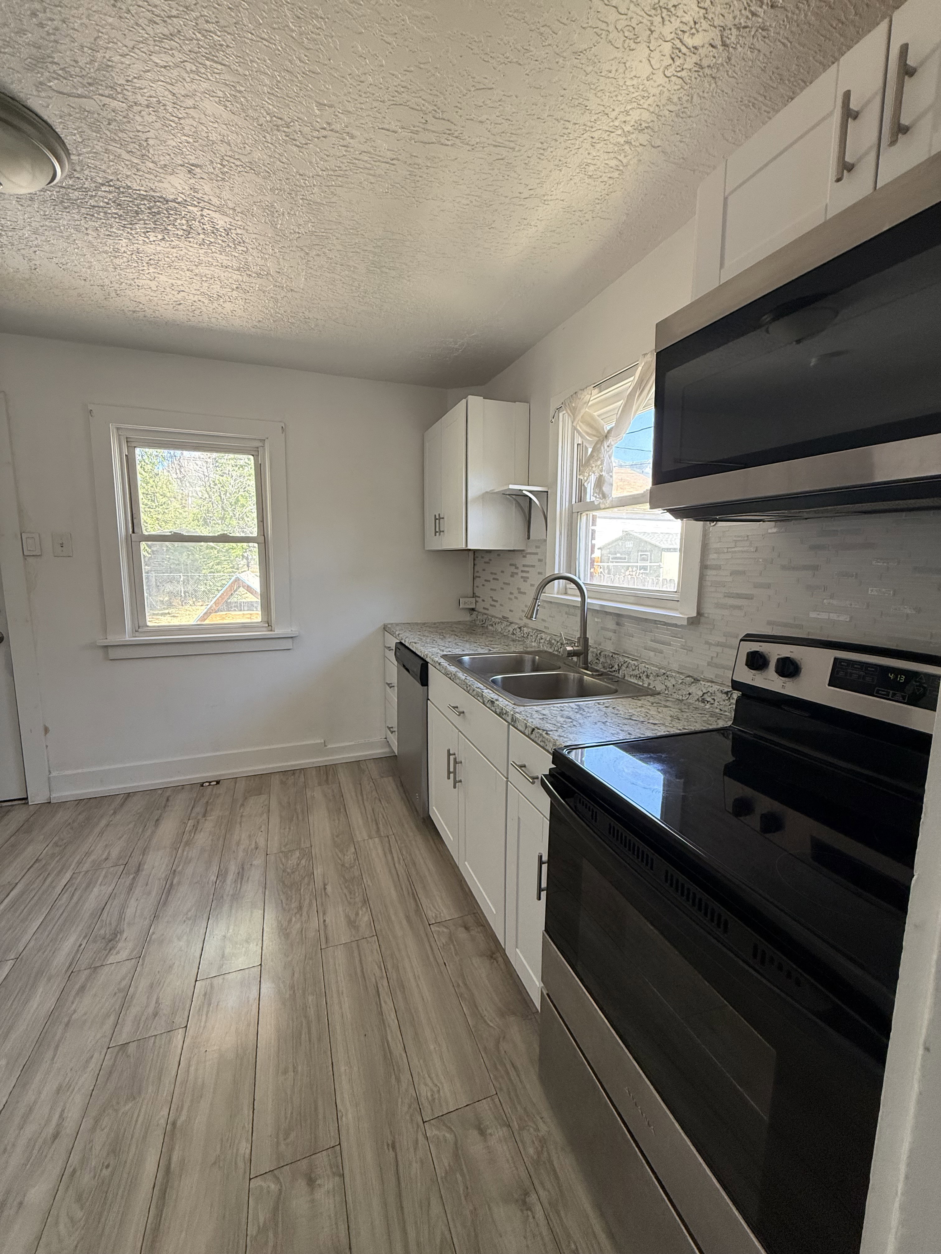 Kitchen featuring light wood-finish flooring, white cabinetry, speckled countertops, a subway tile backsplash, and stainless steel appliances
