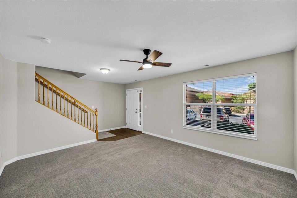 Spacious living area featuring neutral carpeting, light-toned walls, and a contemporary ceiling fan