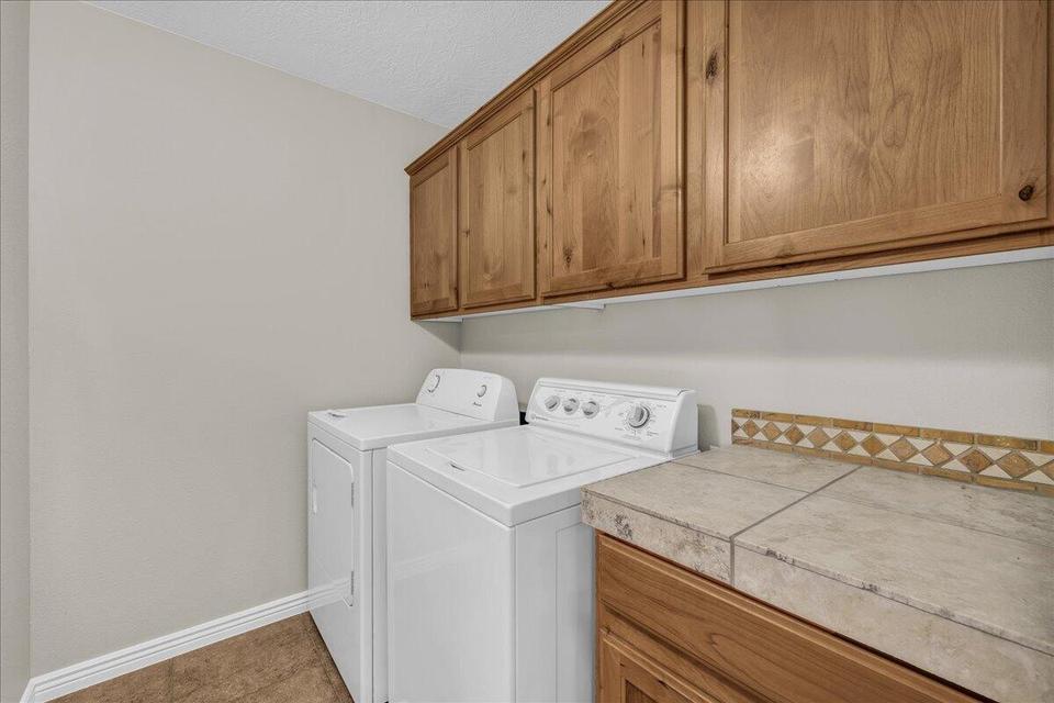 Laundry area featuring wood-finish cabinetry, tile countertop, decorative tile backsplash, and light-toned flooring