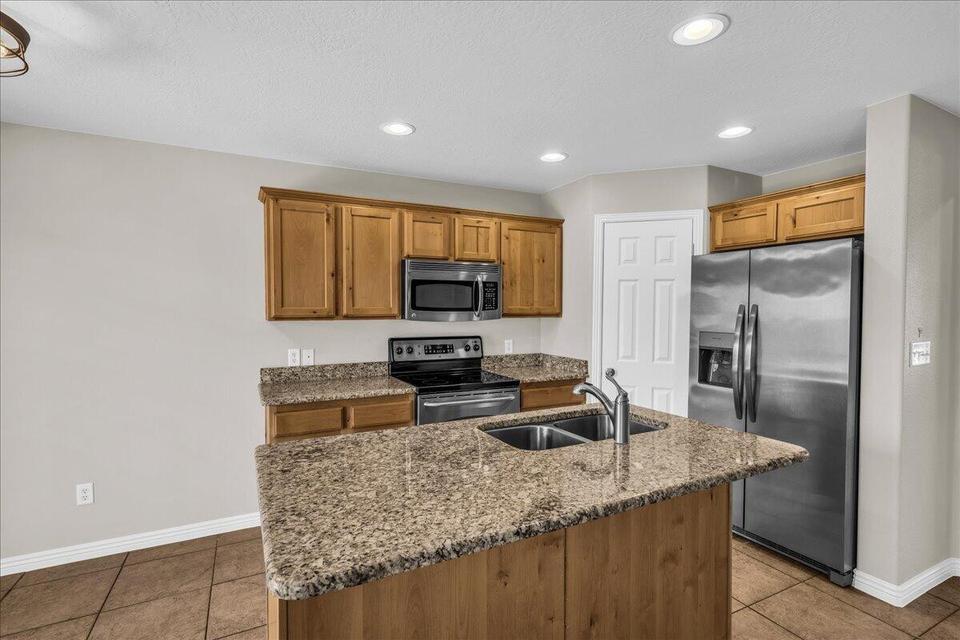 Kitchen featuring a central island with a double basin sink, granite-style countertops, wood cabinetry, stainless steel appliances, and recessed lighting