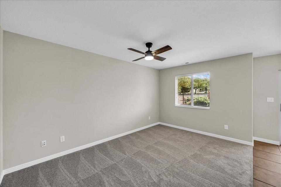 Spacious room featuring neutral paint, gray patterned carpet, a ceiling fan with light, and a window with blinds