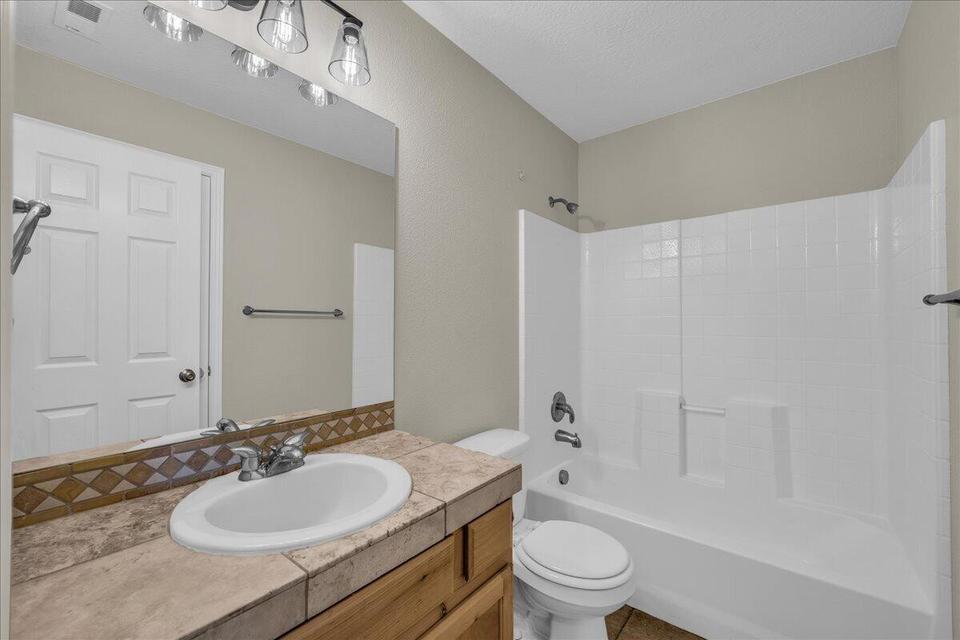 Bathroom featuring a built-in vanity with a tiled countertop and integrated sink, a large wall-mounted mirror, and a full-size tub with shower