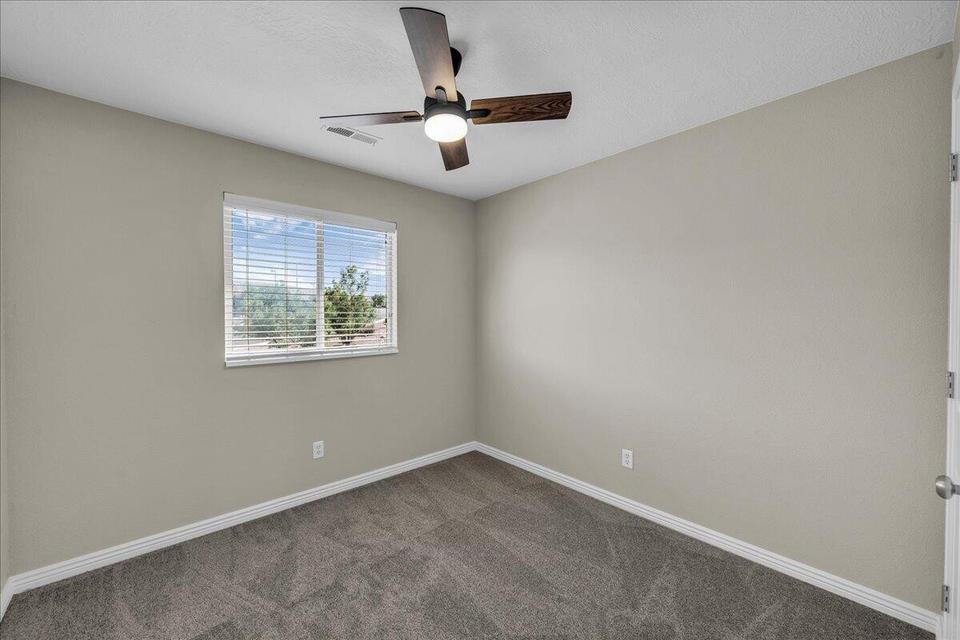 Room featuring neutral-toned walls, gray carpet, a single window with white blinds, and a dark wood ceiling fan with integrated lighting
