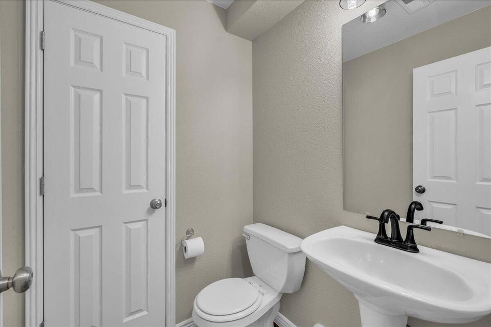 Pedestal sink with a matte black faucet, wall-mounted mirror, and overhead vanity lighting