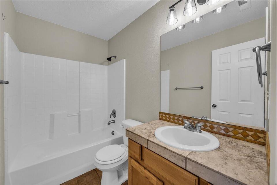 Bathroom featuring a white tub/shower combination, a vanity with a tiled countertop, a built-in sink, and a wall-mounted mirror with overhead lighting